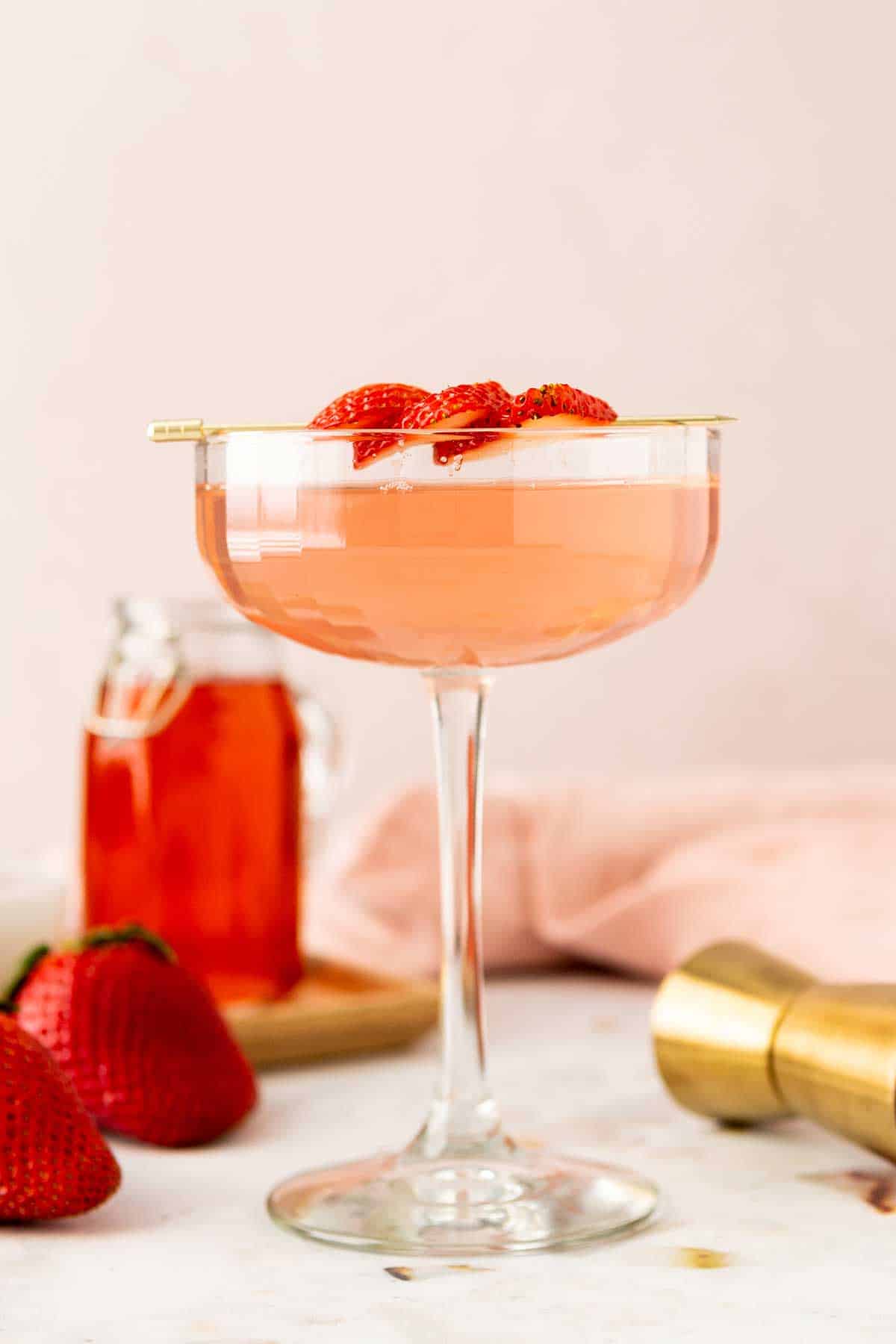 Side view of strawberry martini with syrup and strawberry garnish.