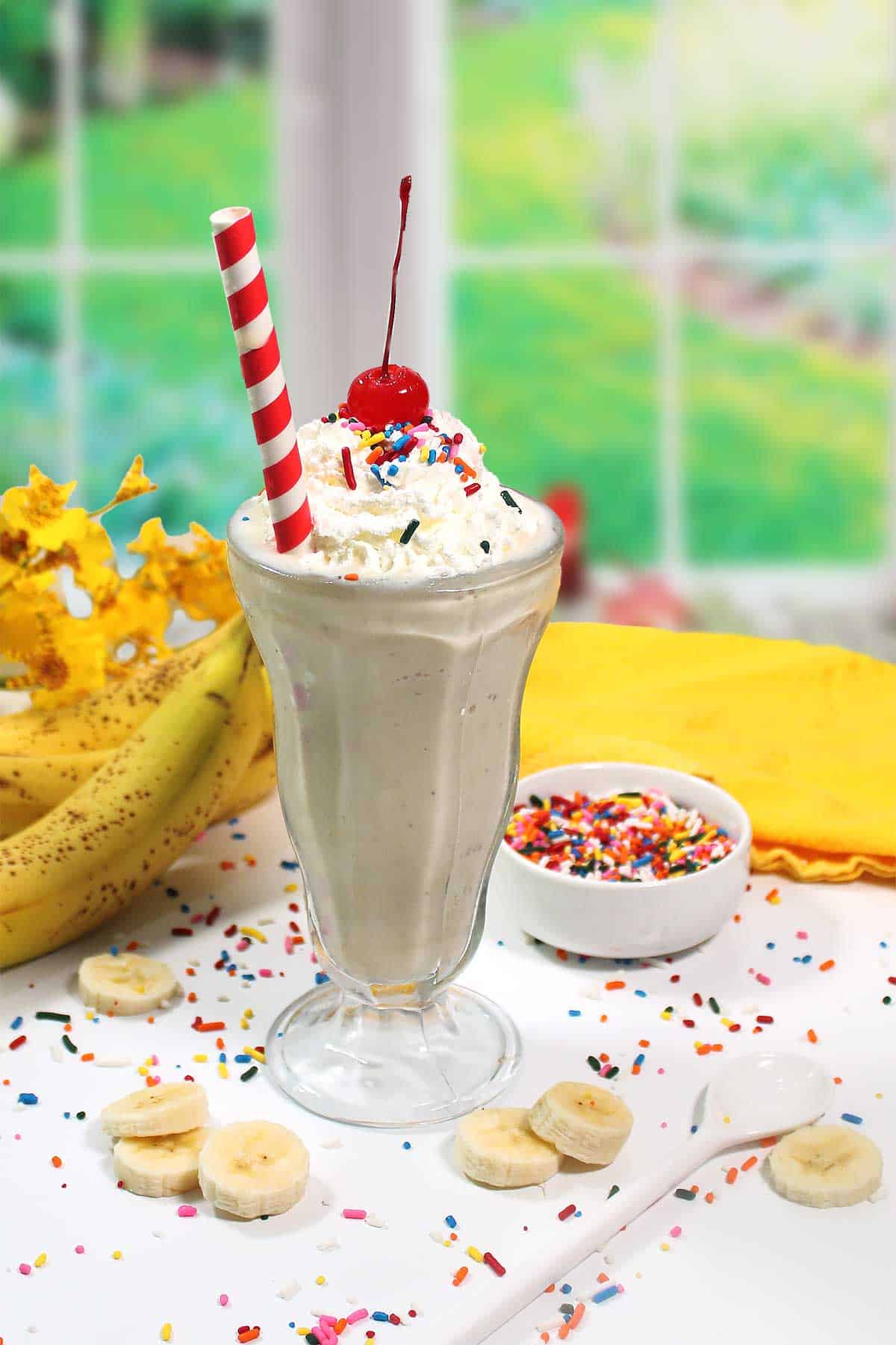 Banana milkshake with whipped cream, cherry and straw by window.