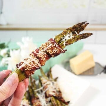 Holding a bacon wrapped asparagus bundle.