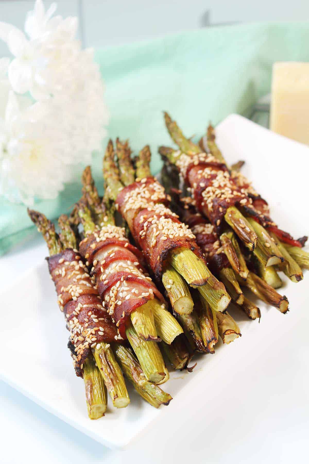 Bacon wrapped asparagus stacked on white platter.