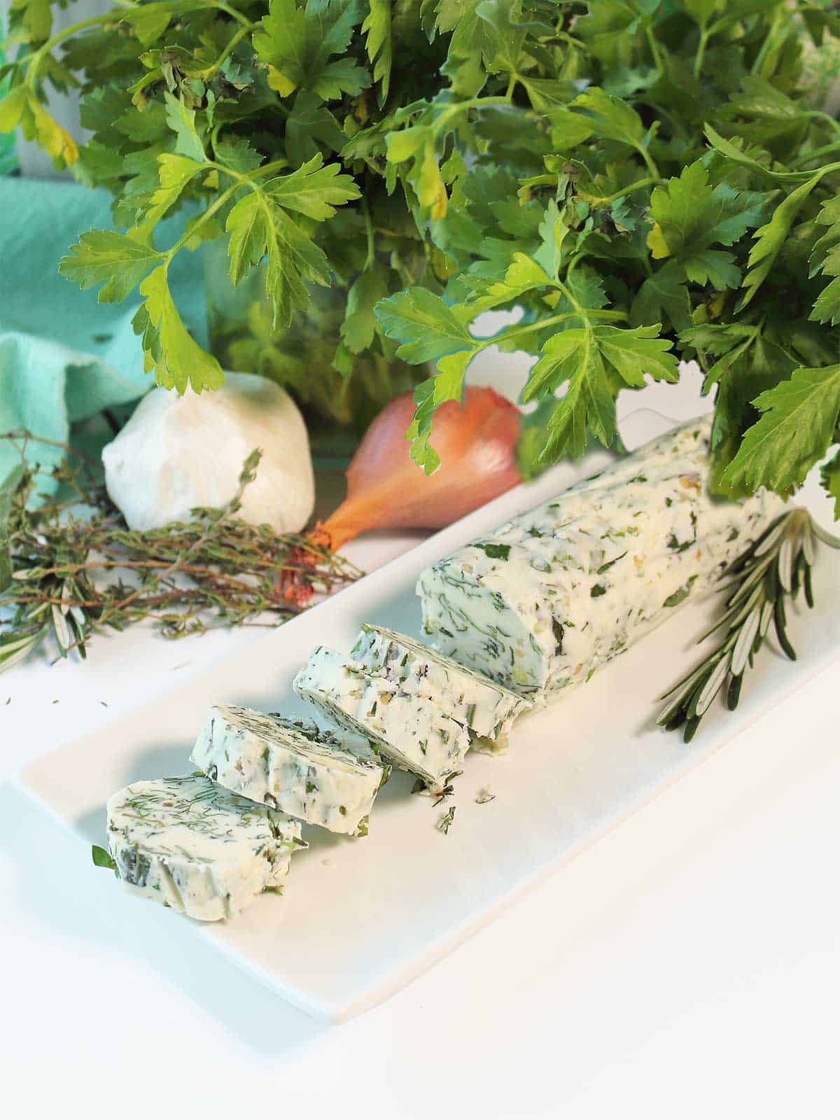 Sliced garlic herb compound butter on white platter.