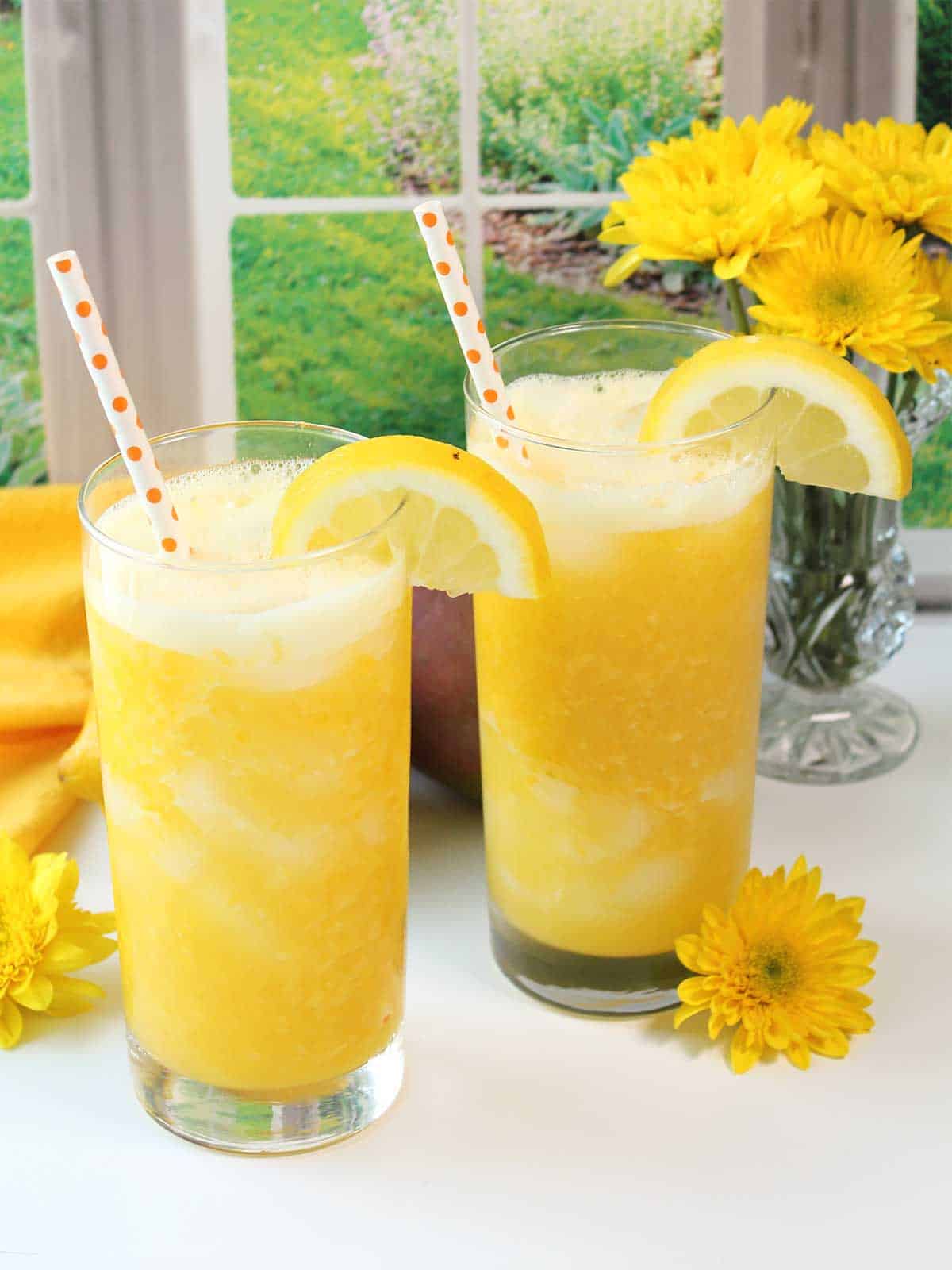 Two glasses of mango lemonade with lemon garnish and straw.