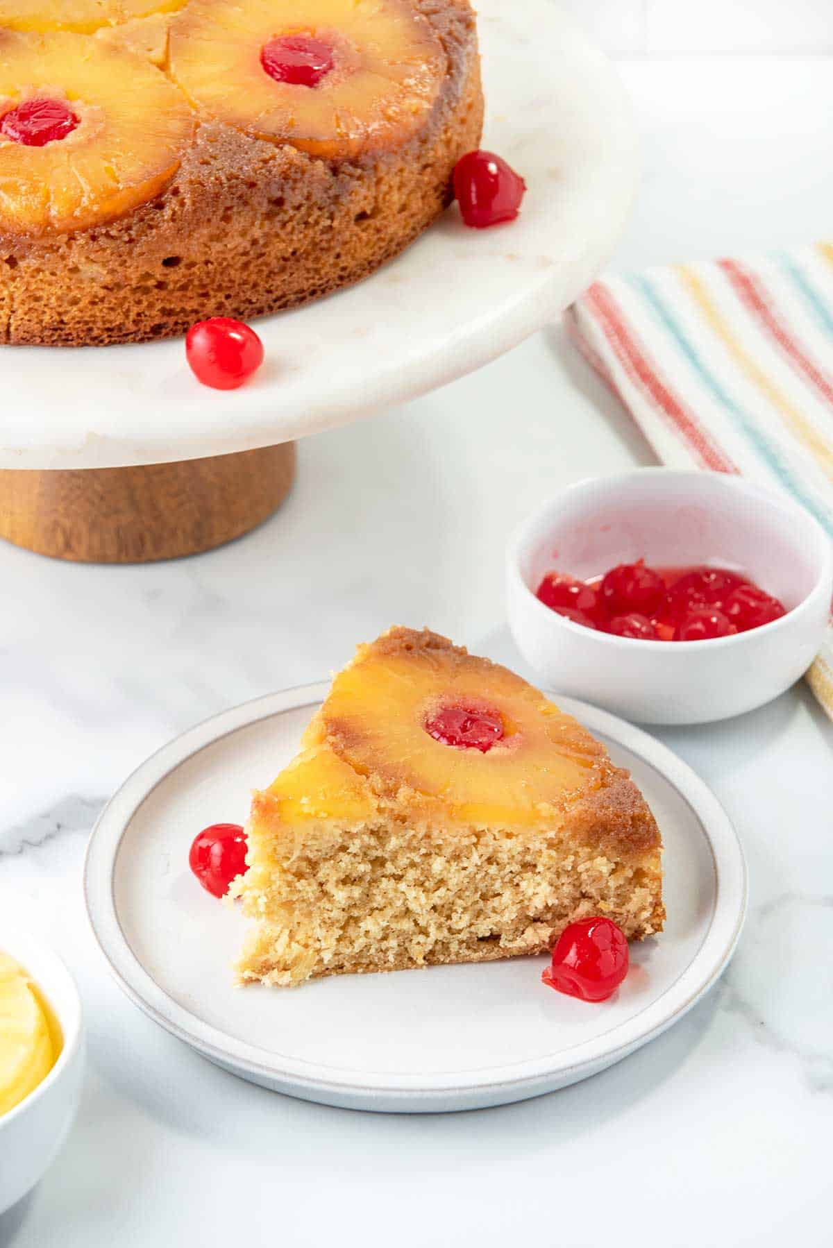 Slice of upside down cake on plate with full cake on cake stand.