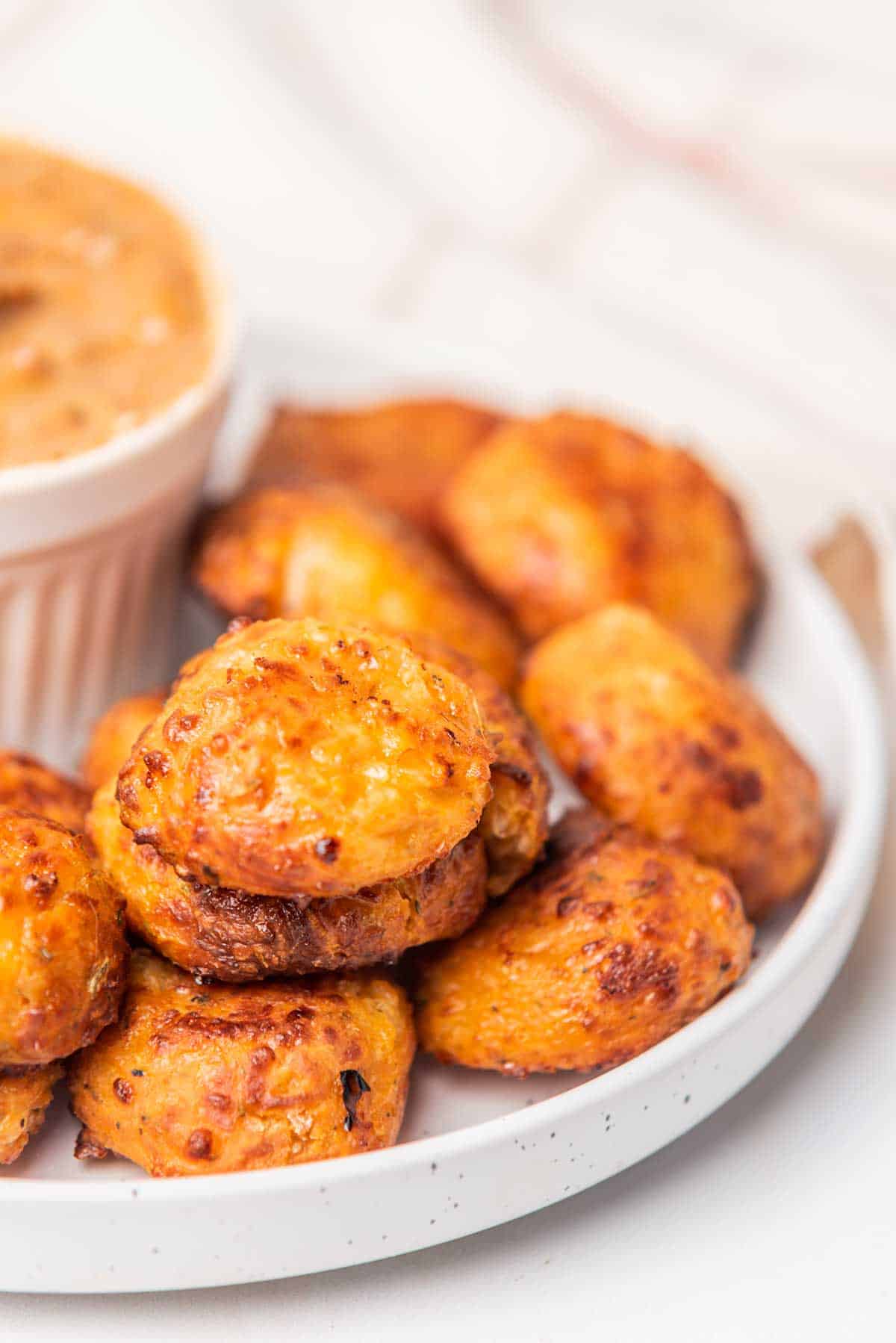 Piled crispy cheese bites on white plate with dip.