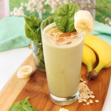 Banana oatmeal smoothie in tall glass on wooden board.