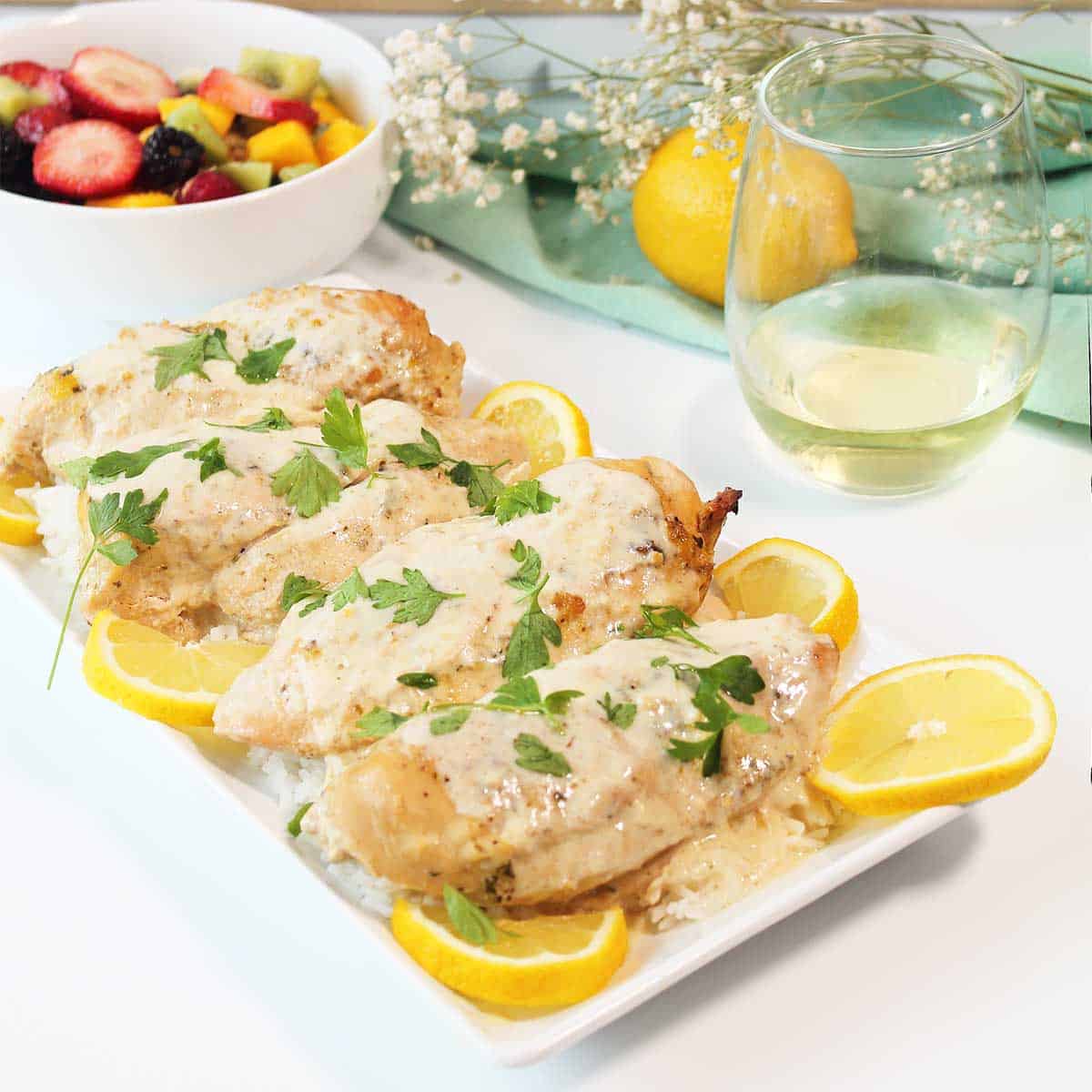 Serving platter of crockpot lemon pepper chicken over rice with drizzle of lemon sauce.