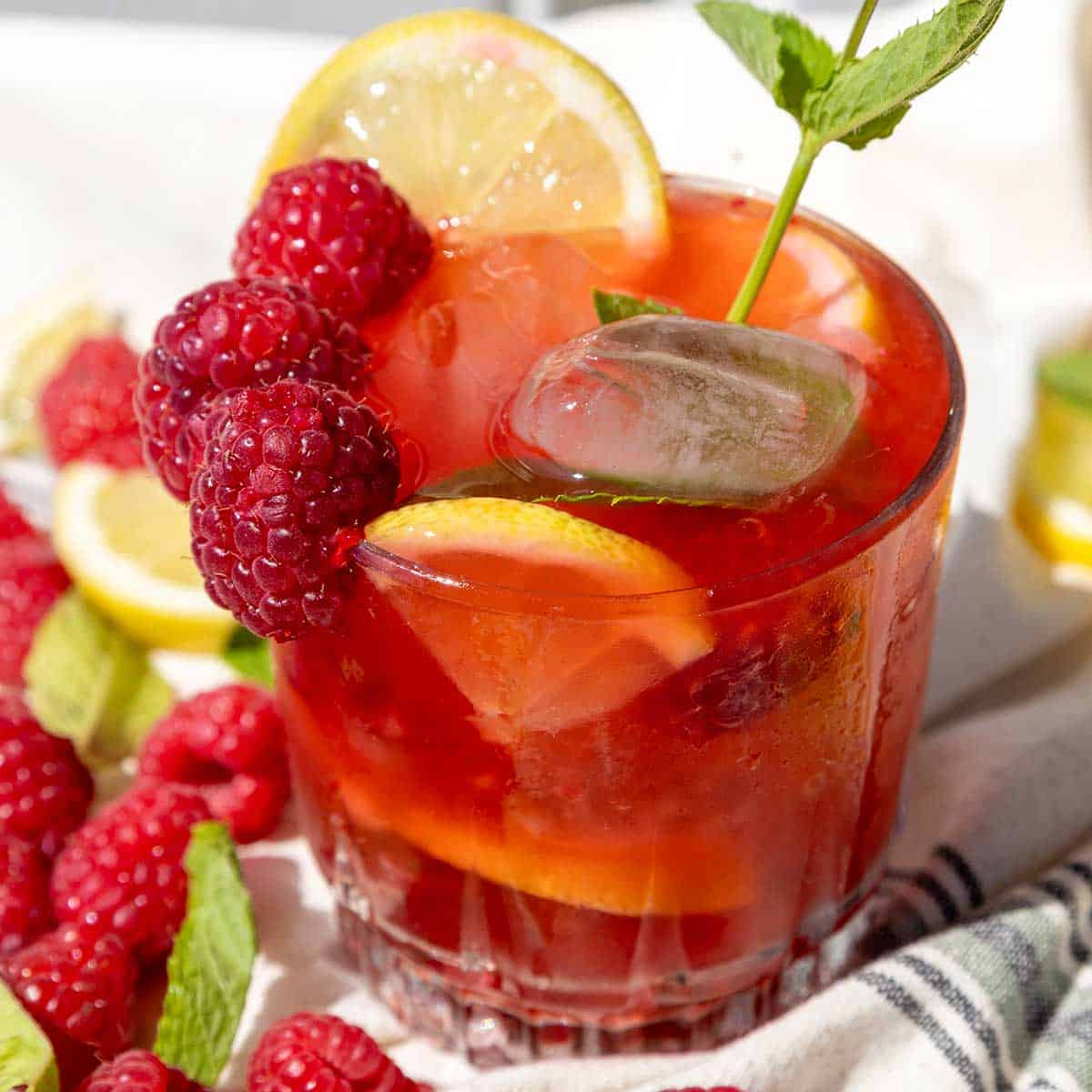 Raspberry Mojito Mocktail in glass with raspberries and lemon on rim.