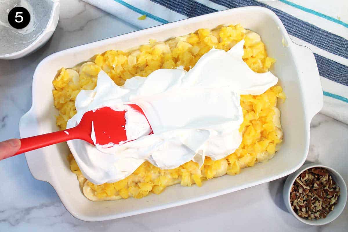 Spreading Cool Whip over pineapple.