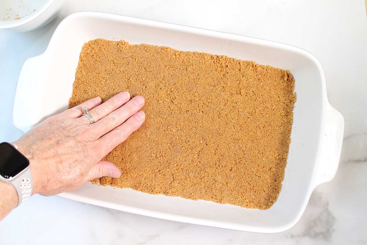 Patting graham cracker crust into baking dish.