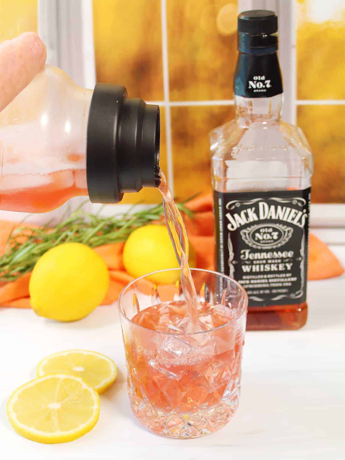 Pouring whiskey and cranberry drink into lowball glass.