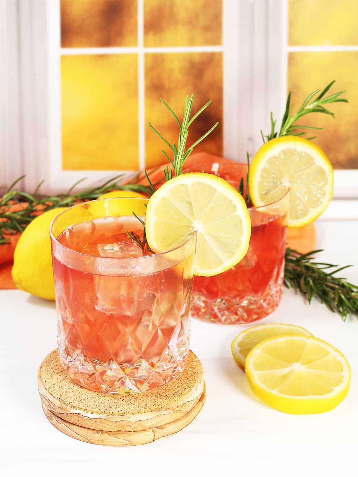 Two garnished cranberry whiskey sour cocktails by window.