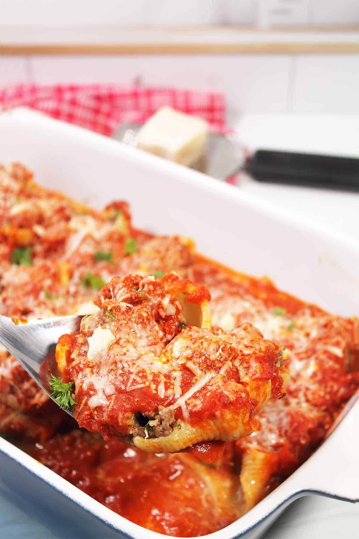 Baked stuffed shells with ground beef on serving spoon.