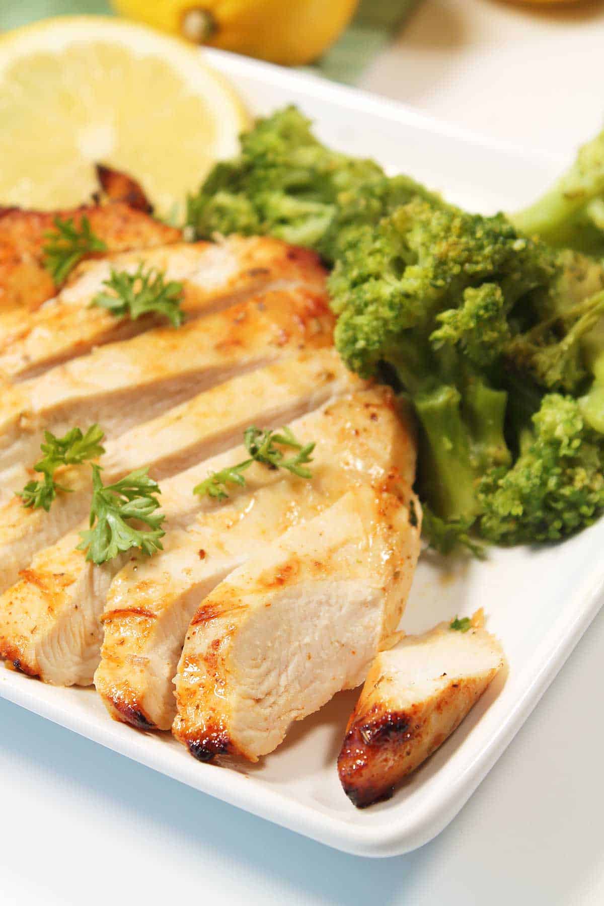 Sliced air fryer chicken breast on dinner plate with broccoli.
