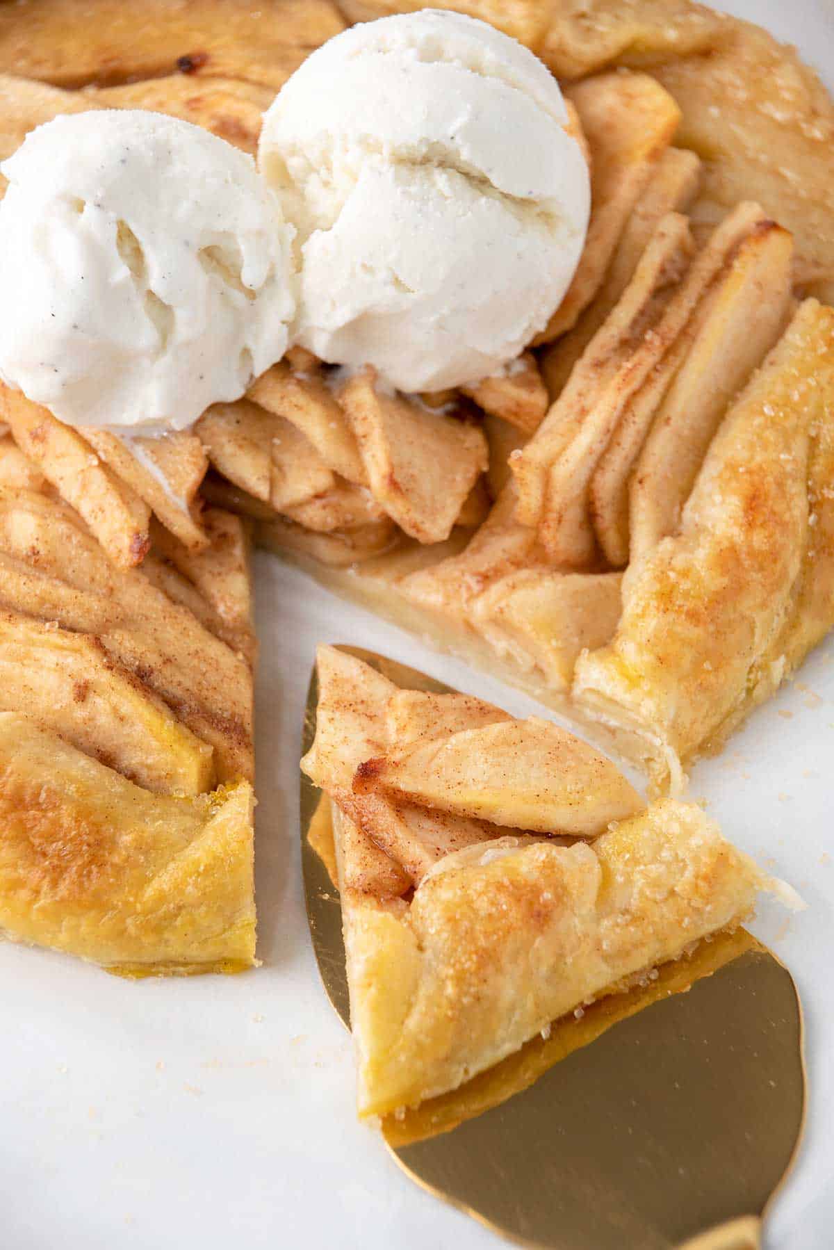 Lifting a slice out of baked apple galette with puff pastry.