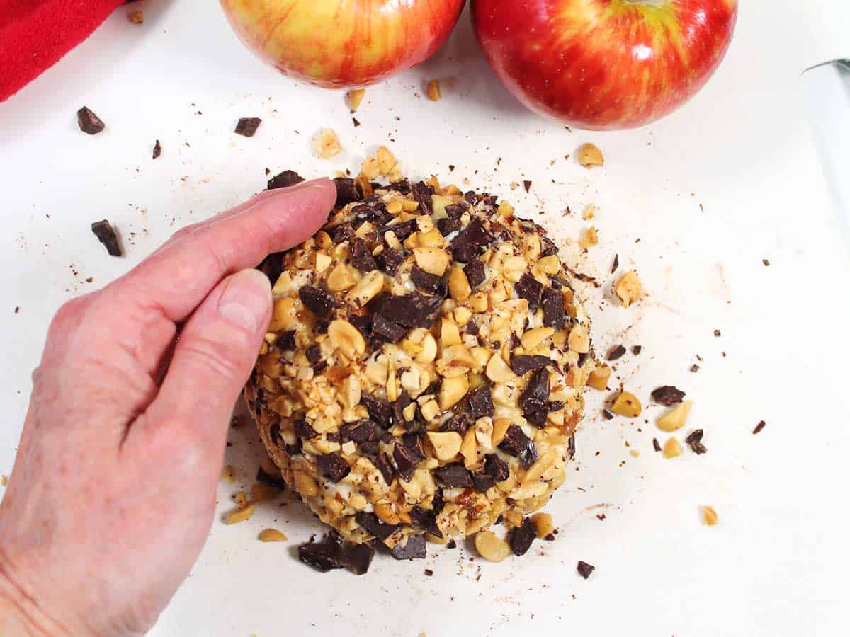 Patting chopped nuts and chocolate coating around cream cheese cheeseball.