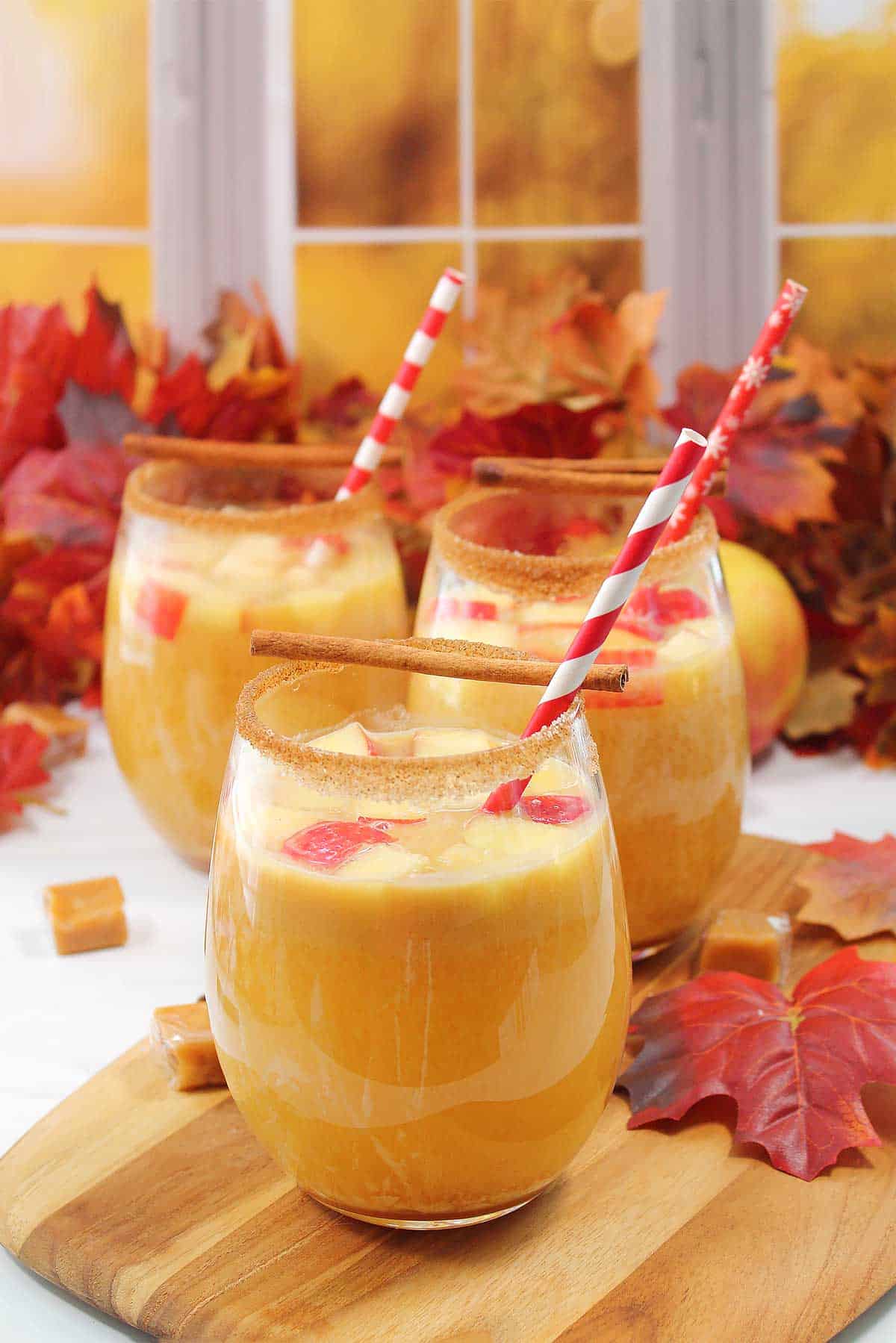 Three glasses of apple cider sangria on wooden board.
