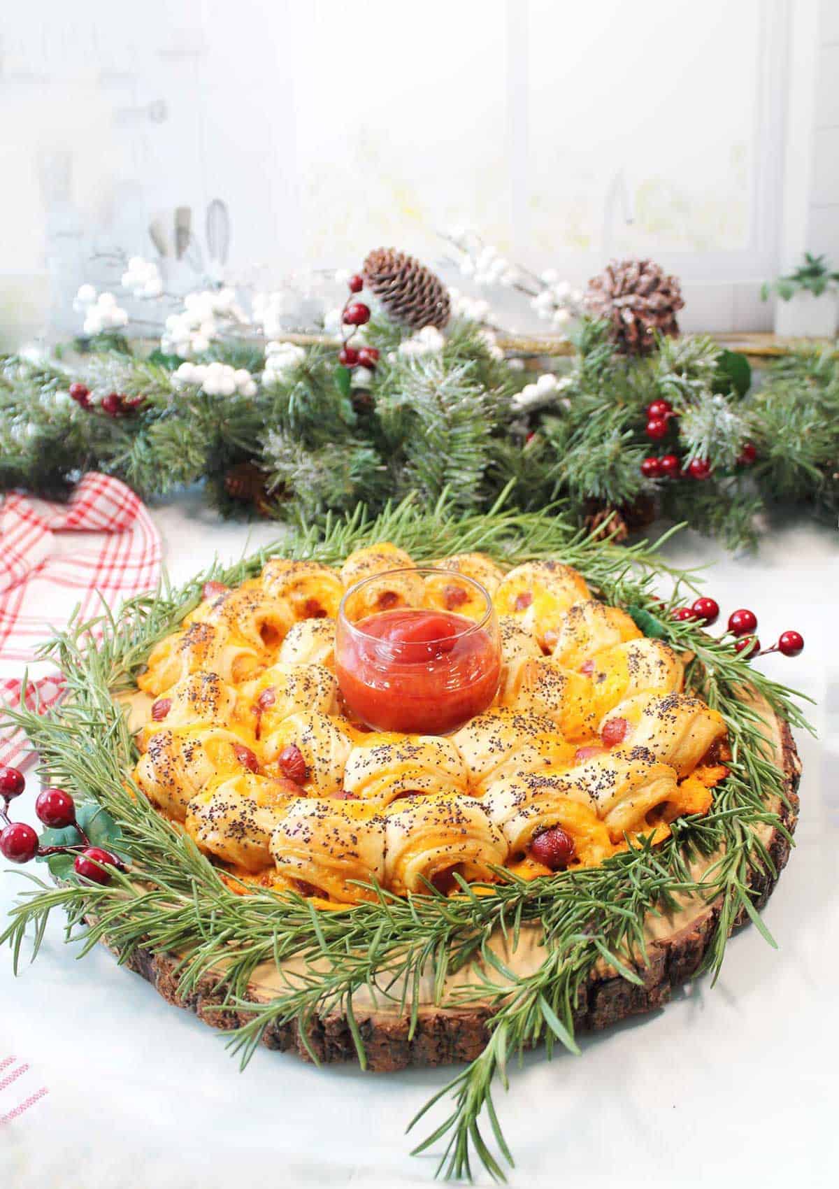 Garnished pigs in a blanket wreath on wooden server.