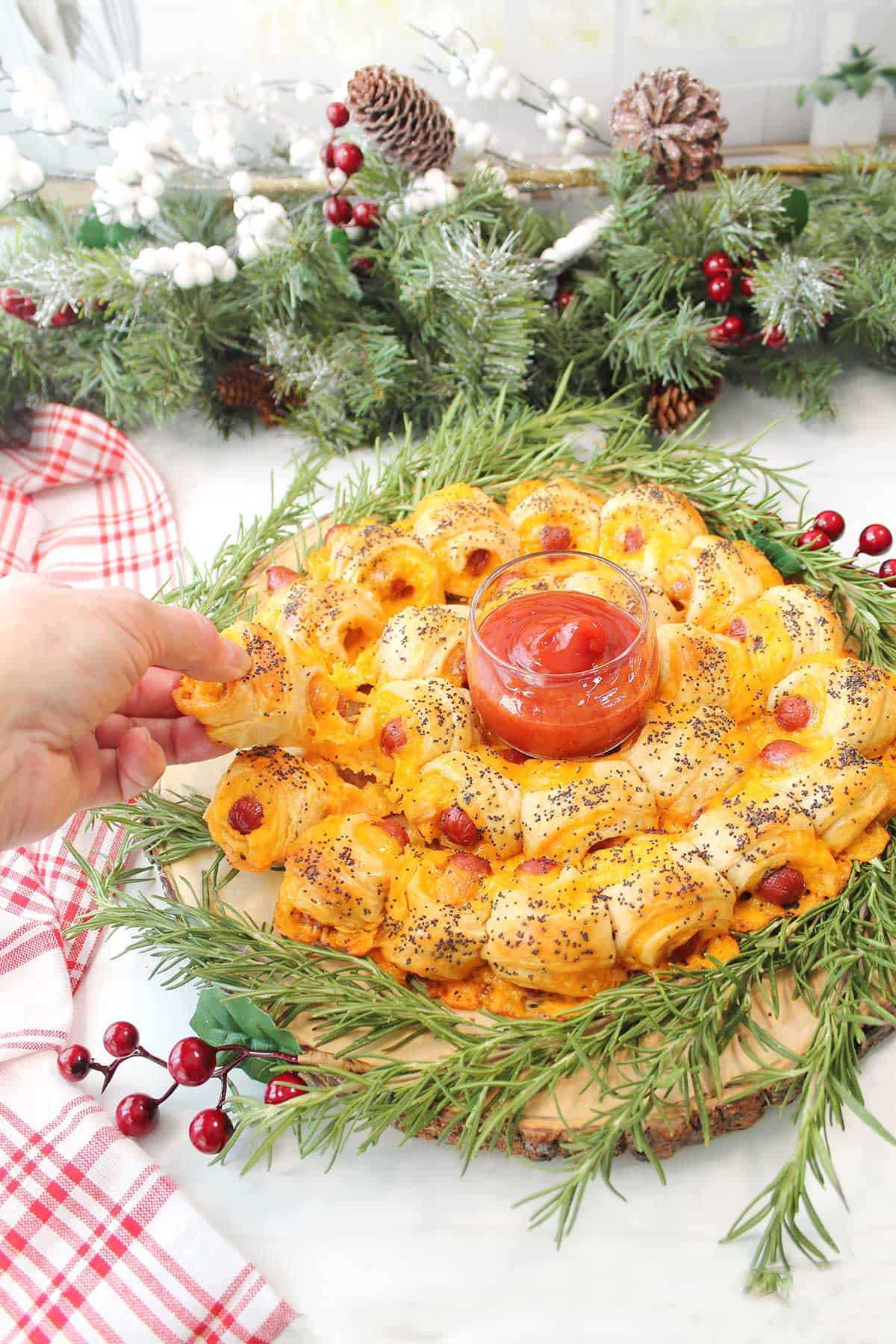 Pulling a pigs in the blanket piece off baked wreath.