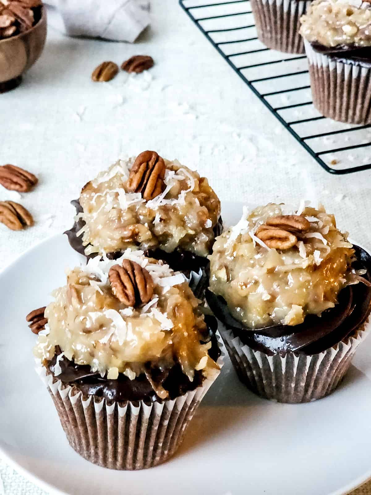Three German chocolate cake cupcakes on white plate.