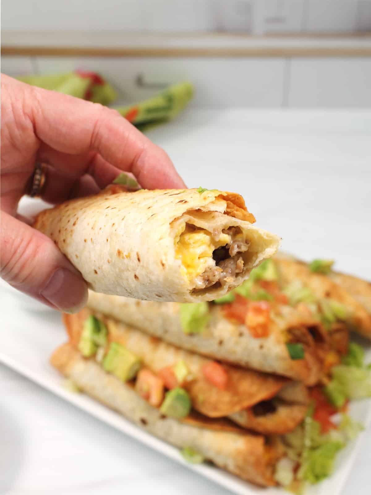 Holding air fried taquitos with bite out of it.