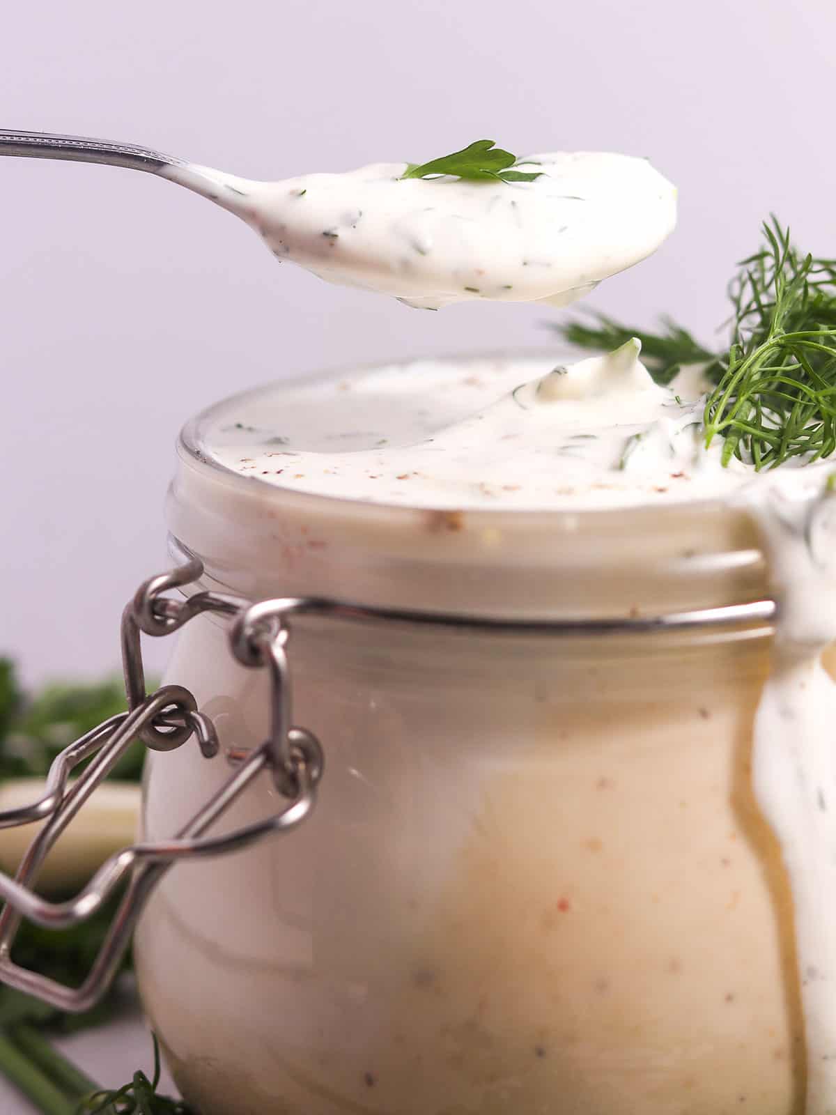 Holding a spoonful over jar of buttermilk ranch dressing.