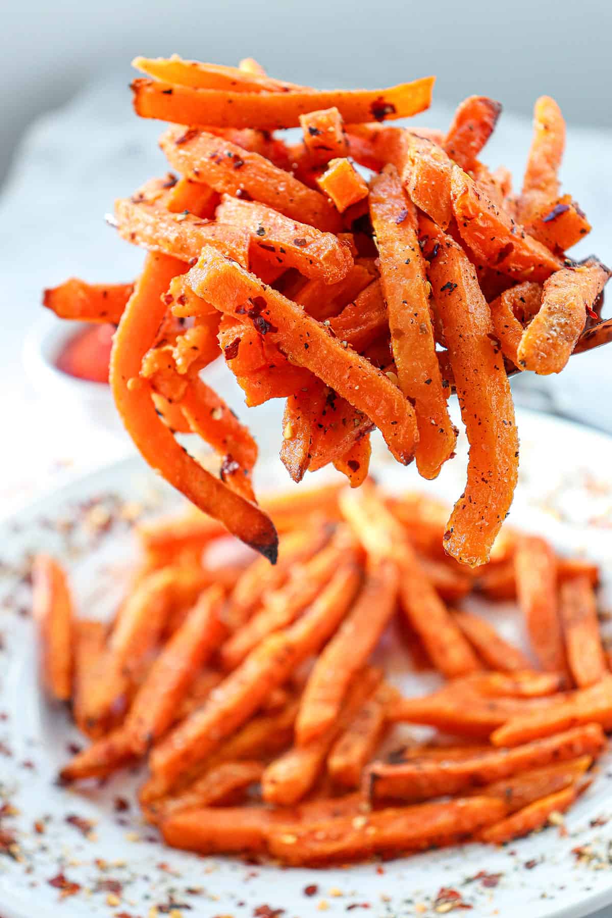 Holding air fryer sweet potato fries over plateful.