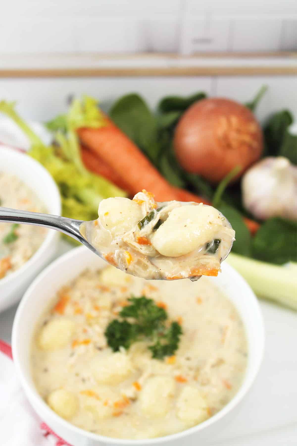Spoonful of slow cooker chicken gnocchi soup over bowl.