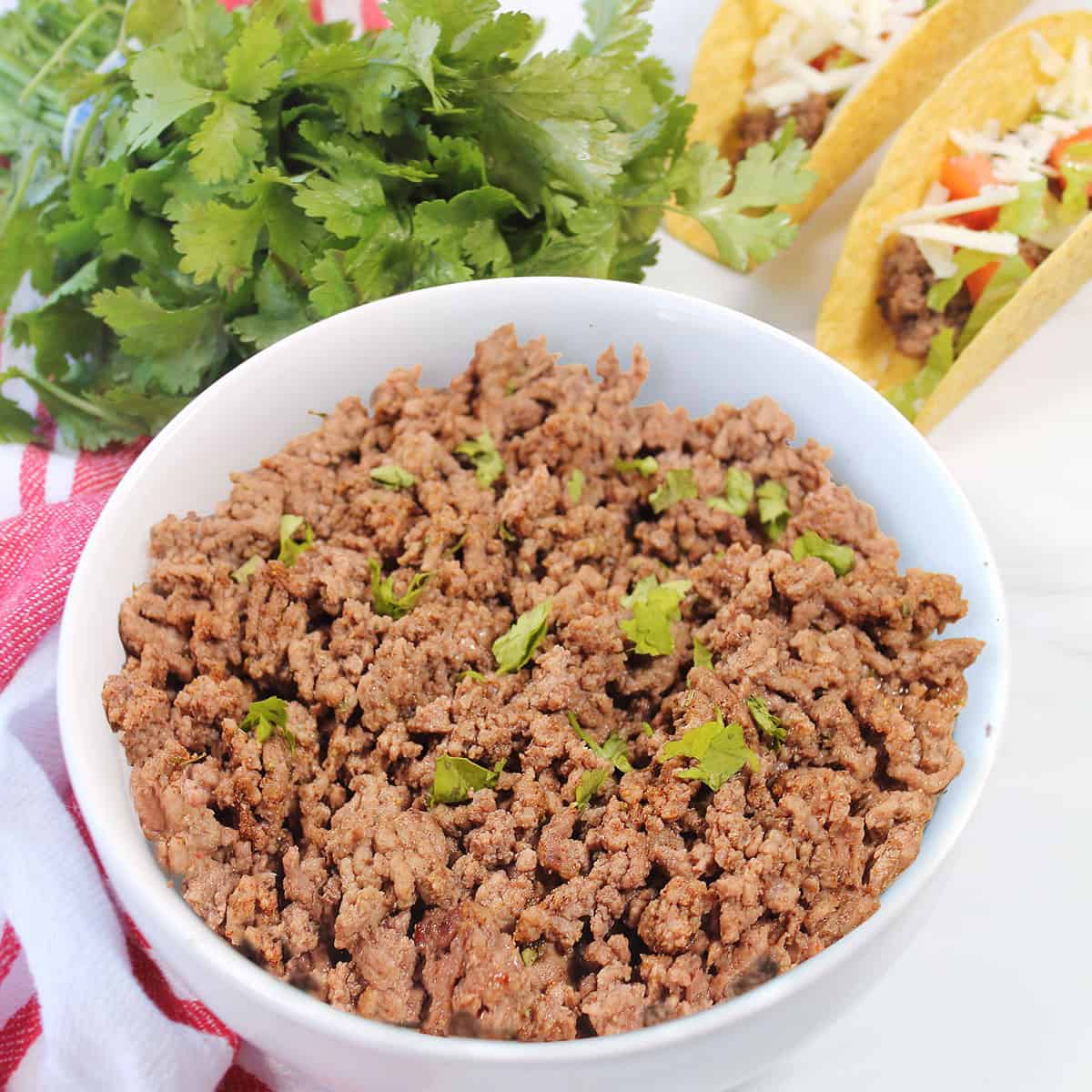 Air fryer ground beef in bowl by tacos and cilantro.