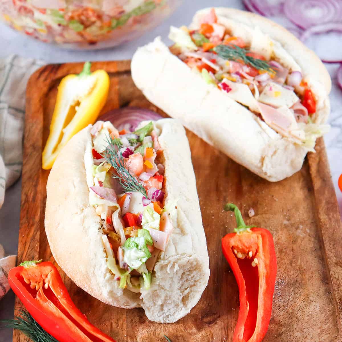 Two chopped Italian sandwiches on cutting board with halved peppers.