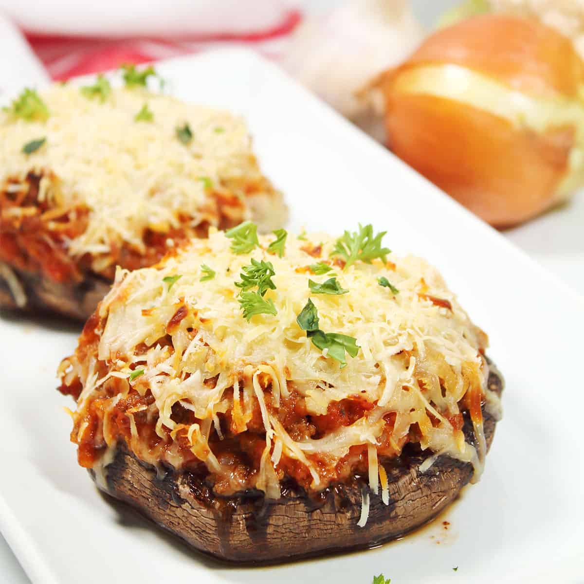 Two stuffed portobello mushroom with ground beef with parsley garnish.
