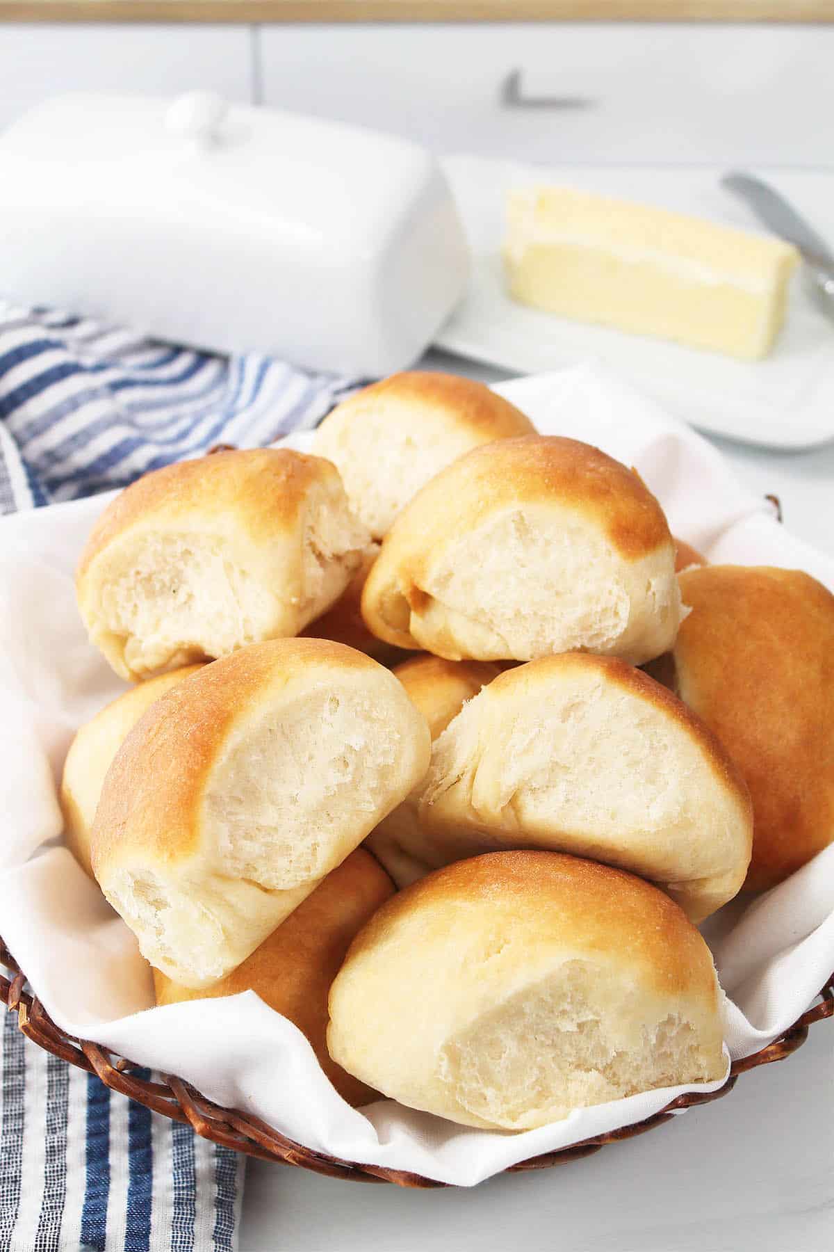 Air fryer dinner rolls in basket with butter dish in back.