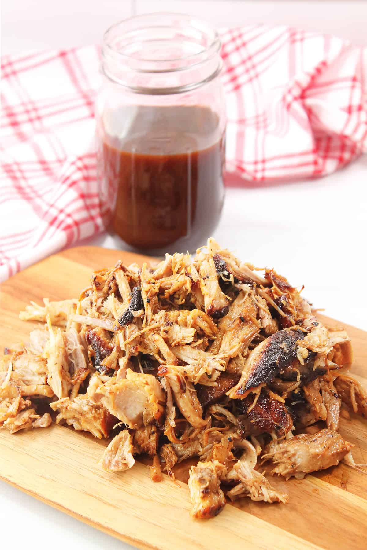 Shredded air fryer pulled pork on cutting board with BBQ sauce in jar.