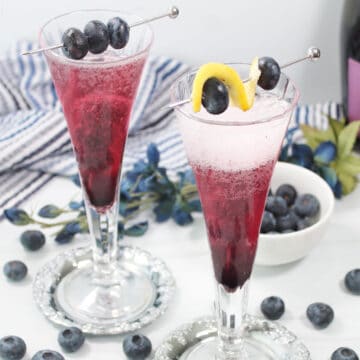 Two blueberry bellini cocktails with garnish.