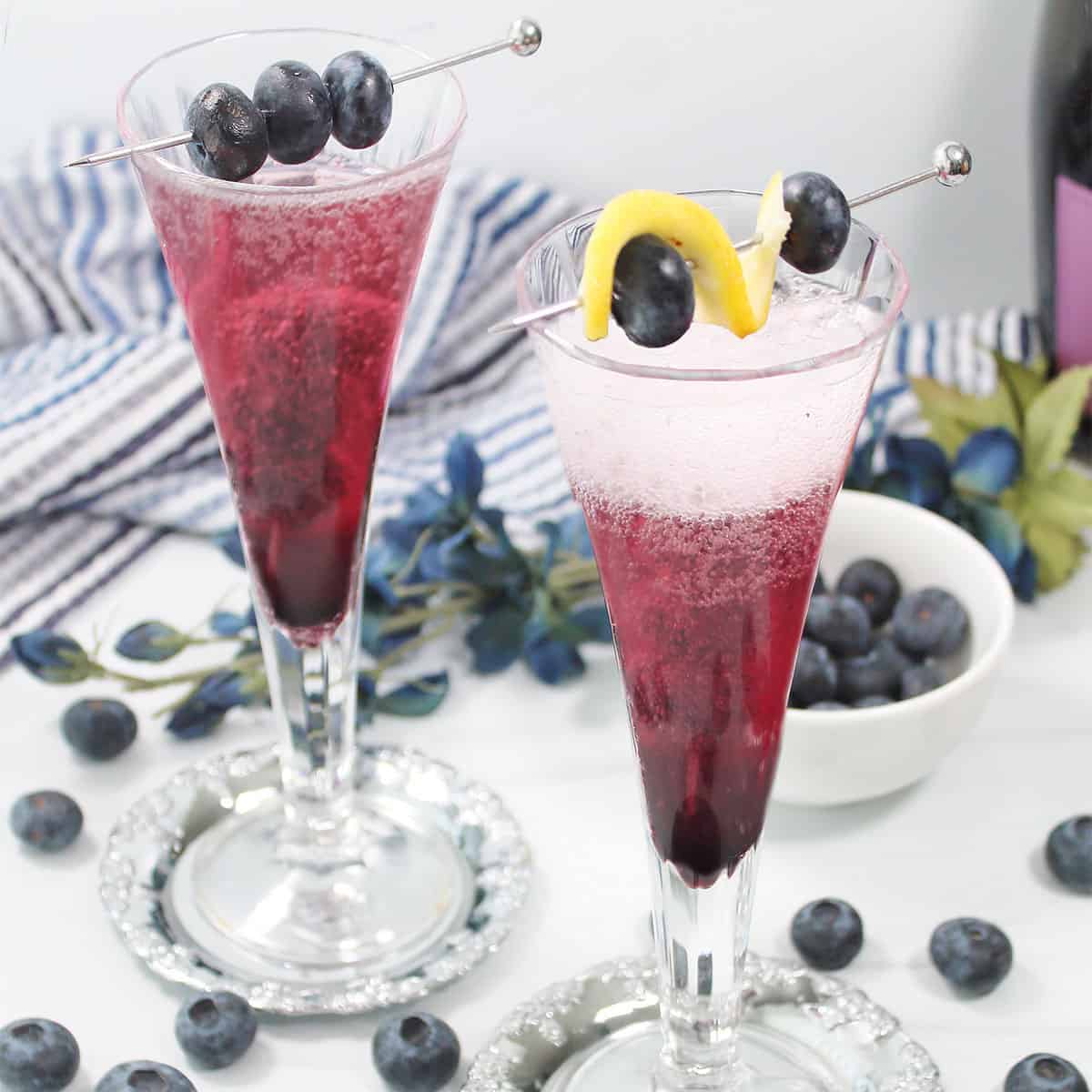 Two blueberry bellini cocktails with garnish.