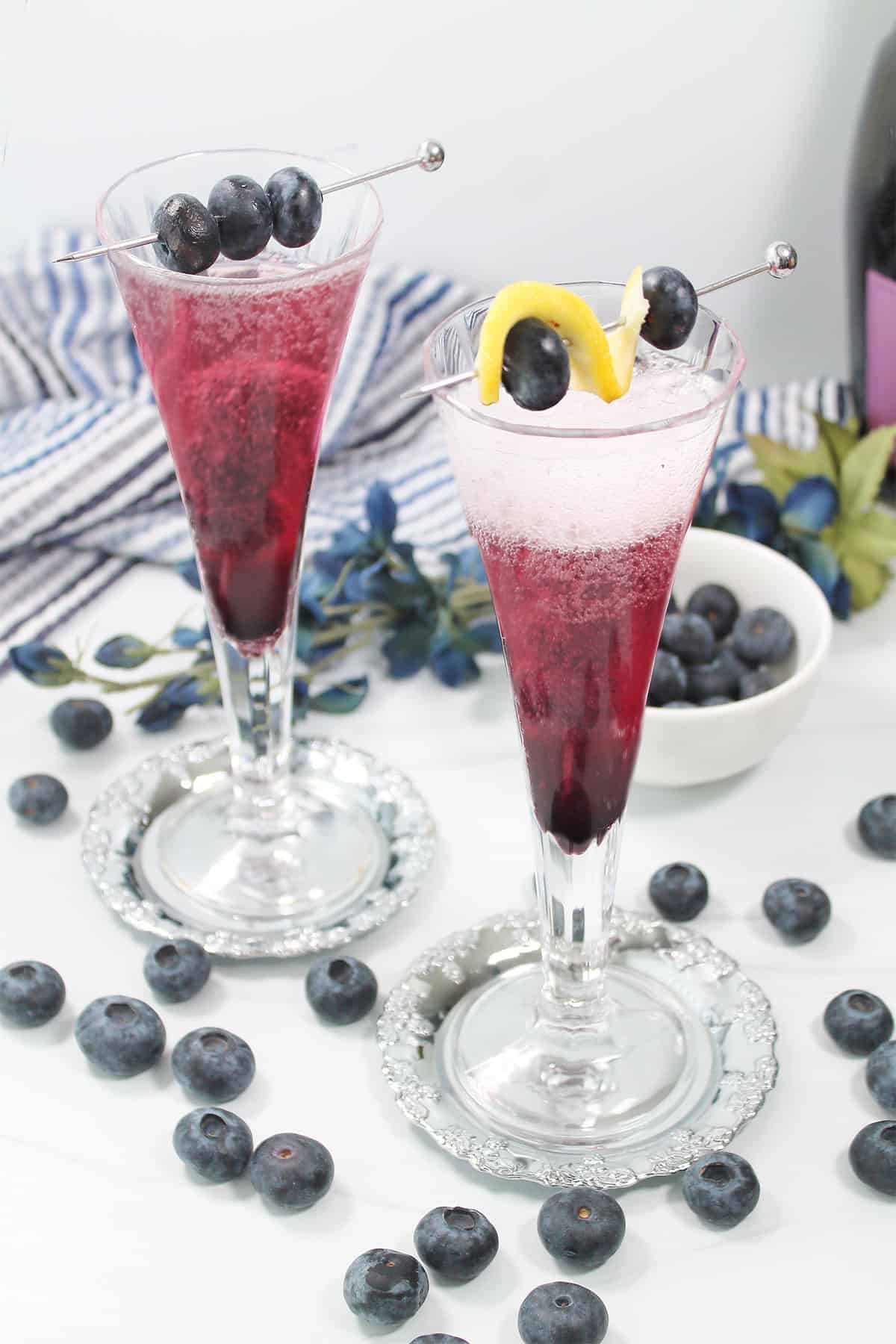 Two blueberry bellini cocktails with garnishes.