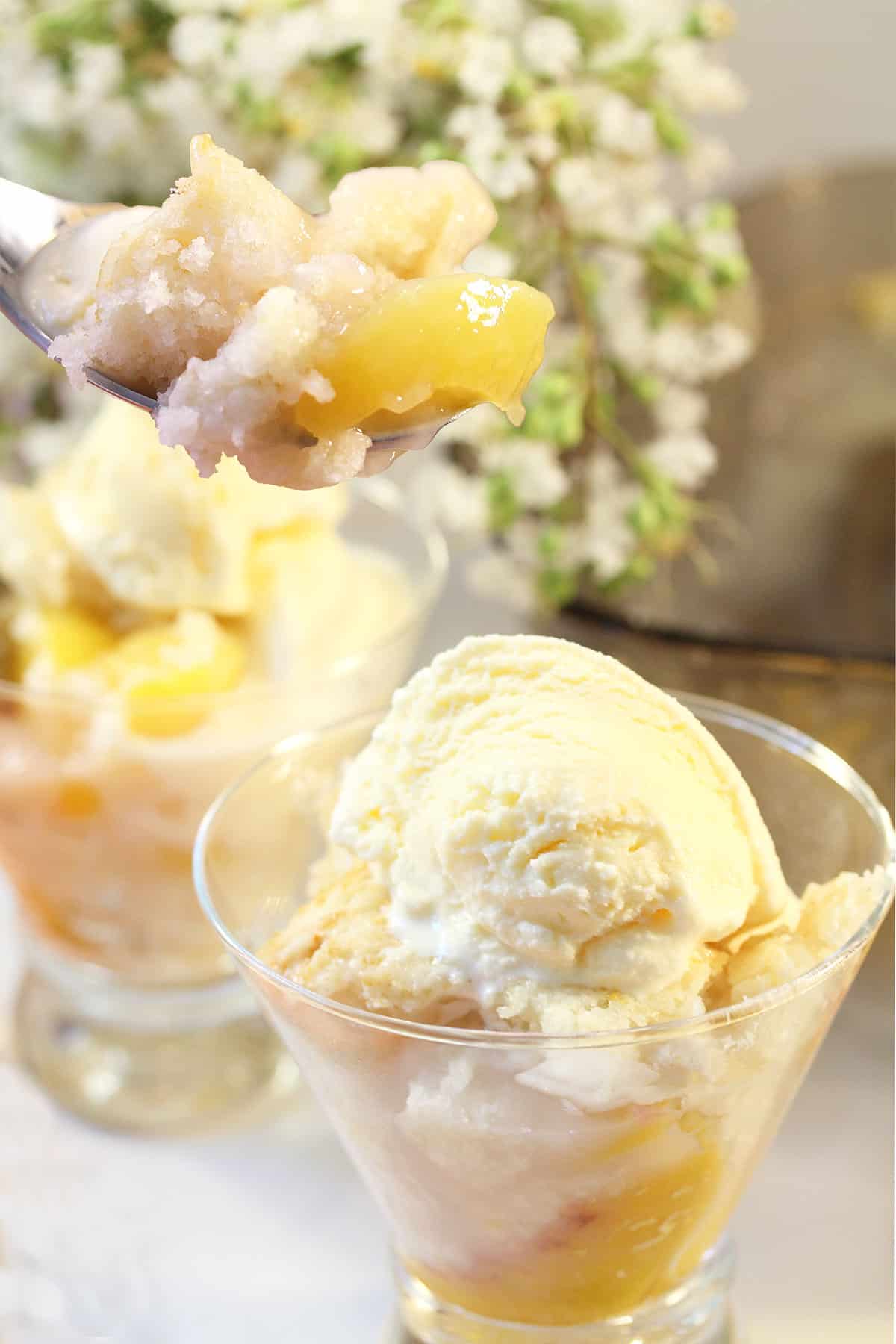 Spoonful of easy peach cobbler with cake mix next to 2 servings.