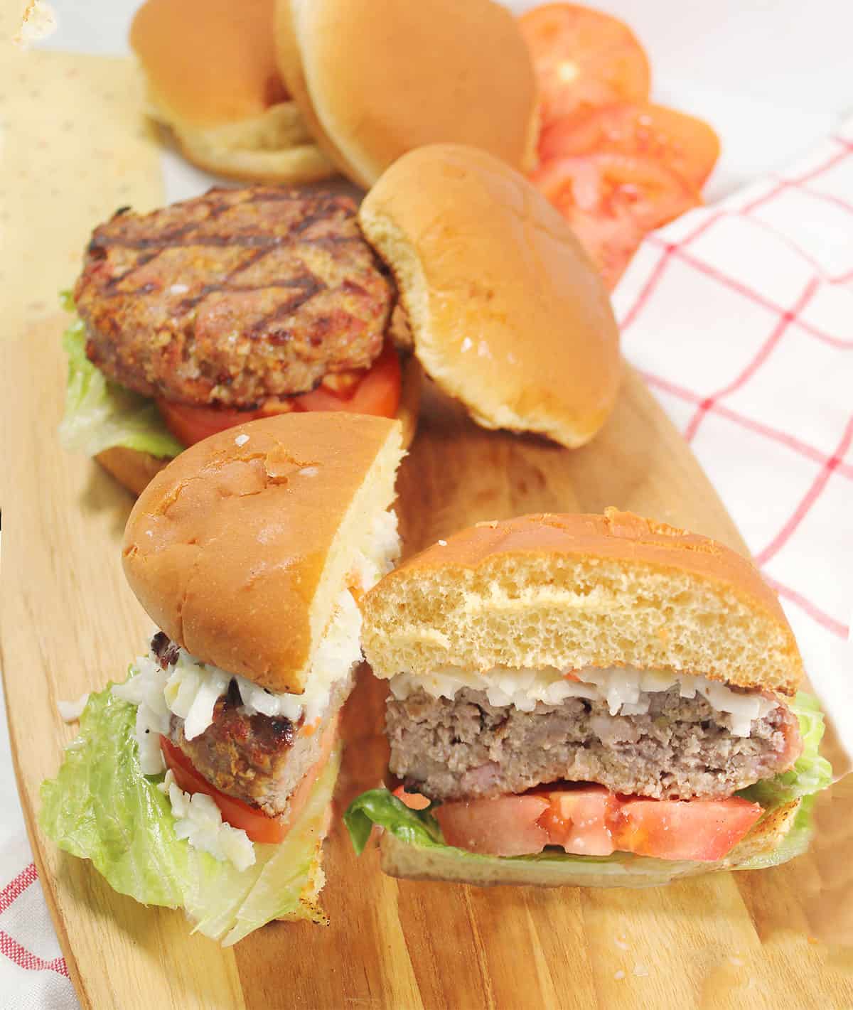 Halved ground pork burgers on wooden board.