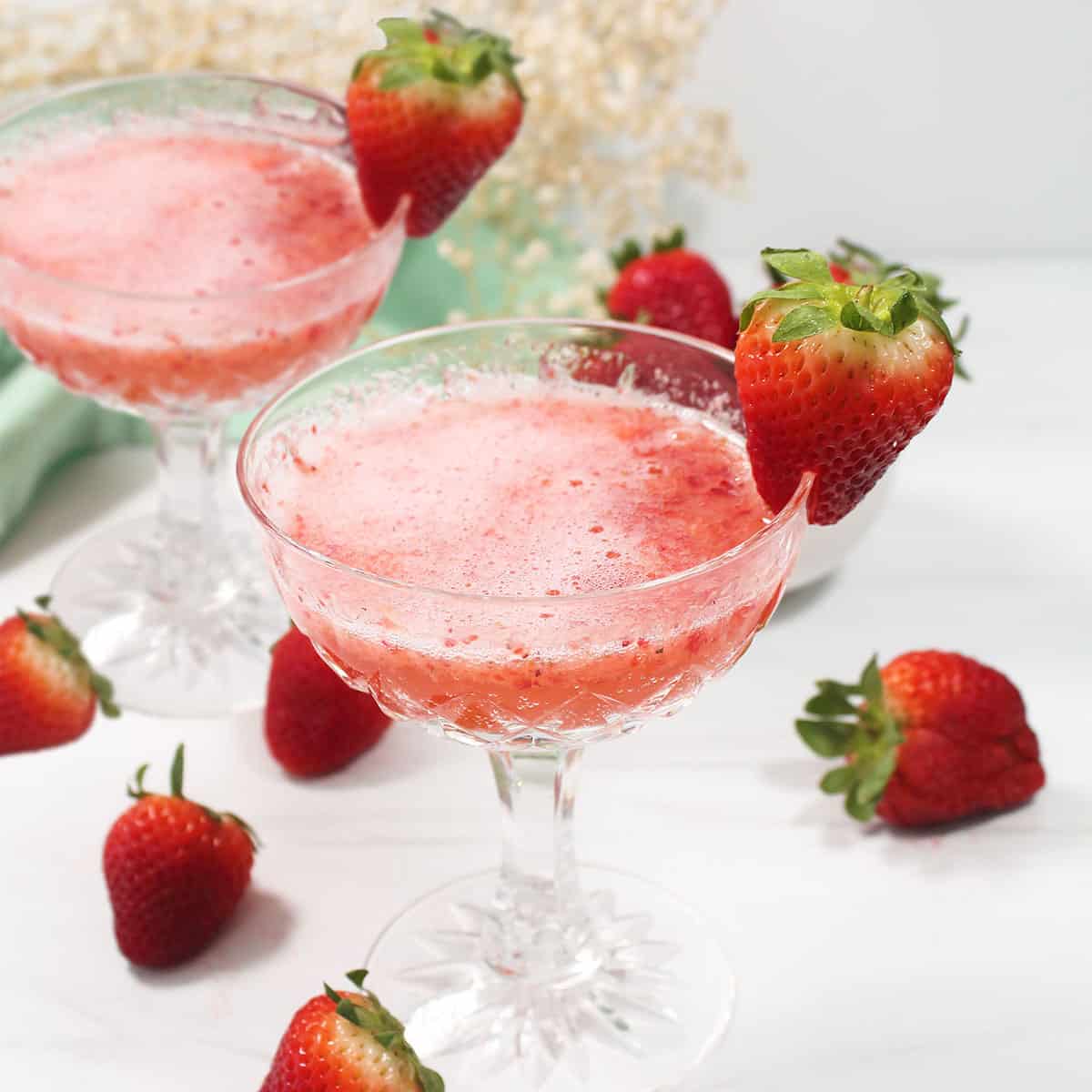 Two strawberry bellini cocktails with scattered strawberries.