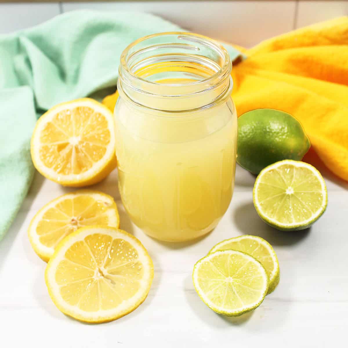 Sweet and Sour Cocktail Mix surrounded by lemons and limes.