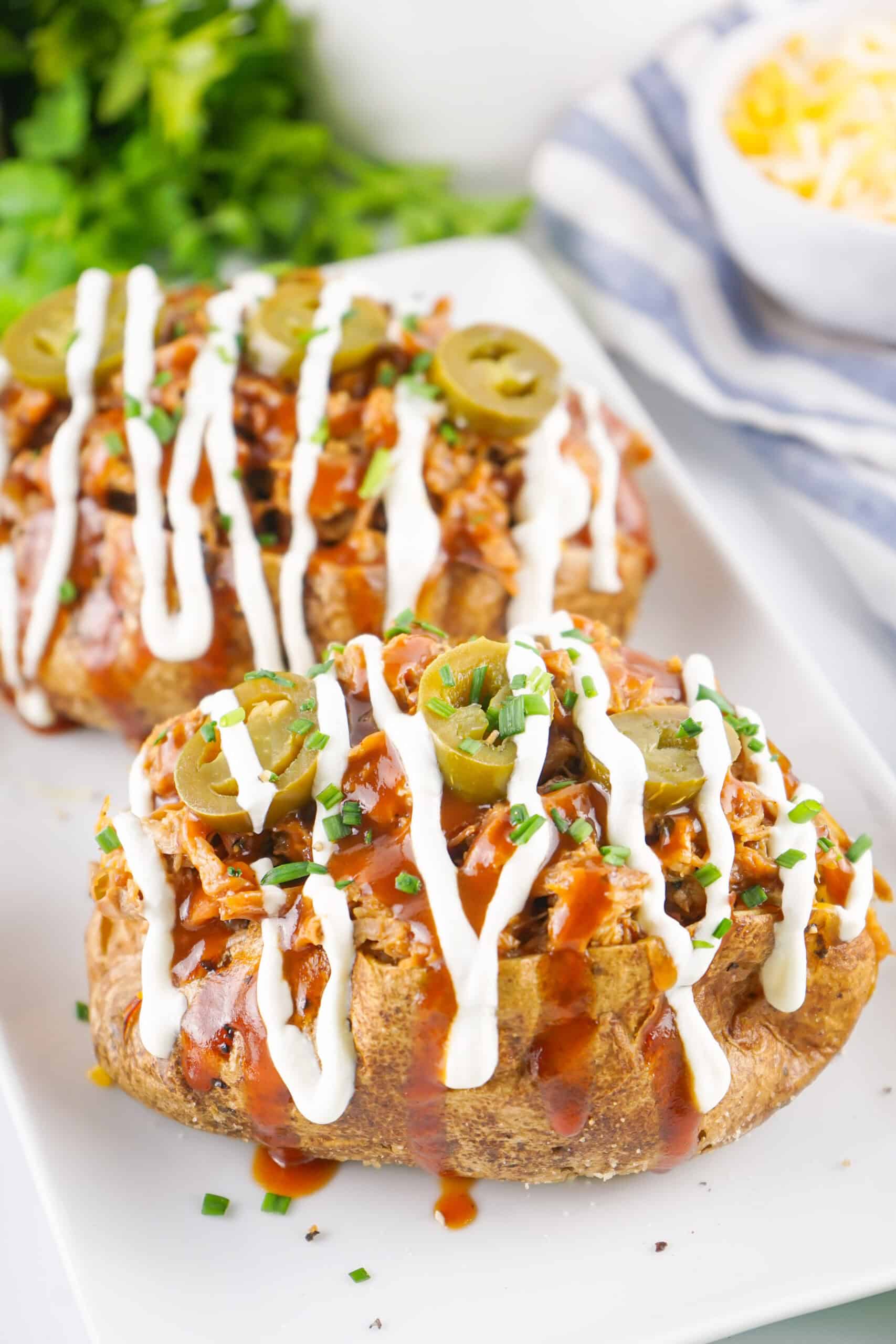 Two Pulled Pork Baked Potatoes on white platter with sour cream drizzle.