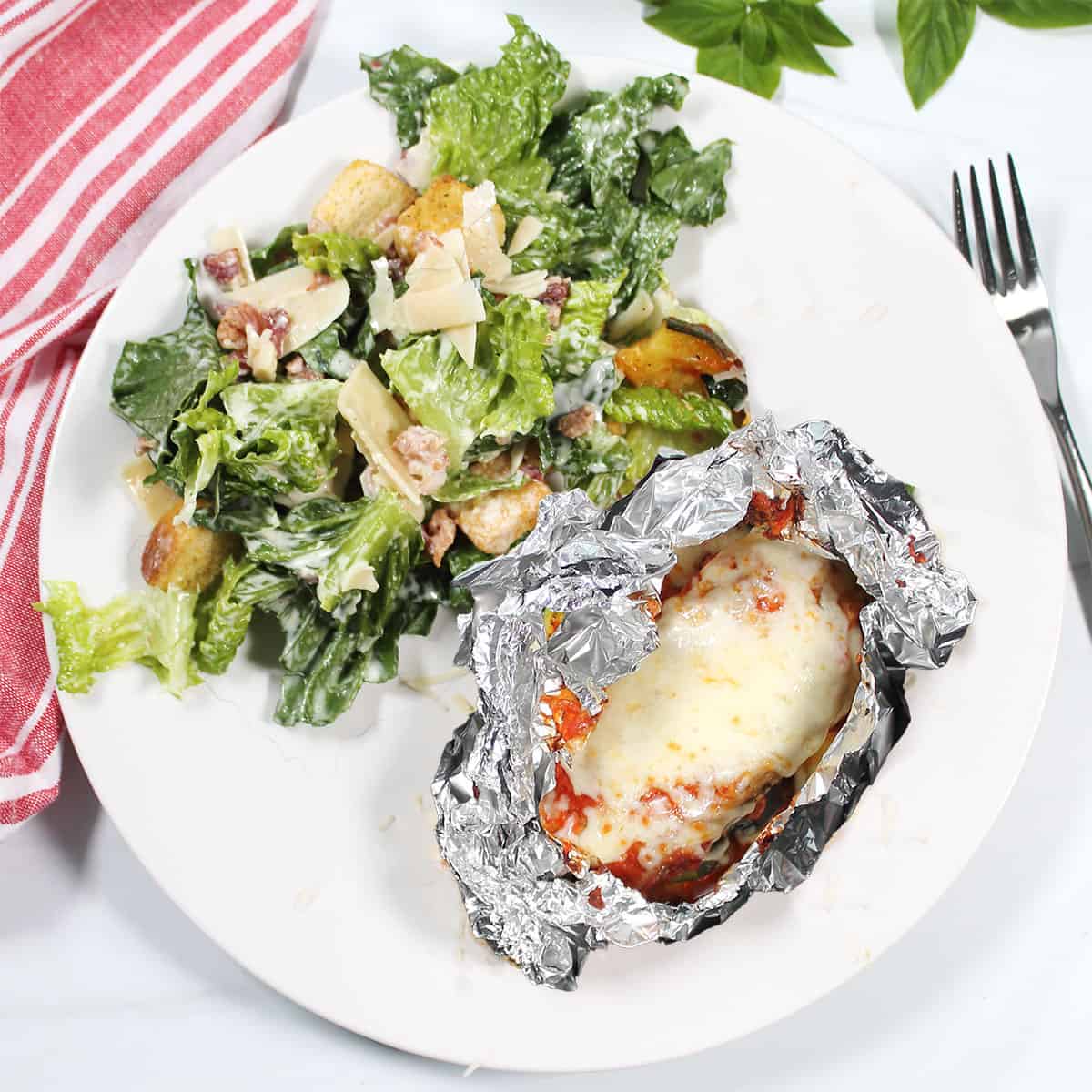 Chicken foil packet dinner in foil, plated with salad.