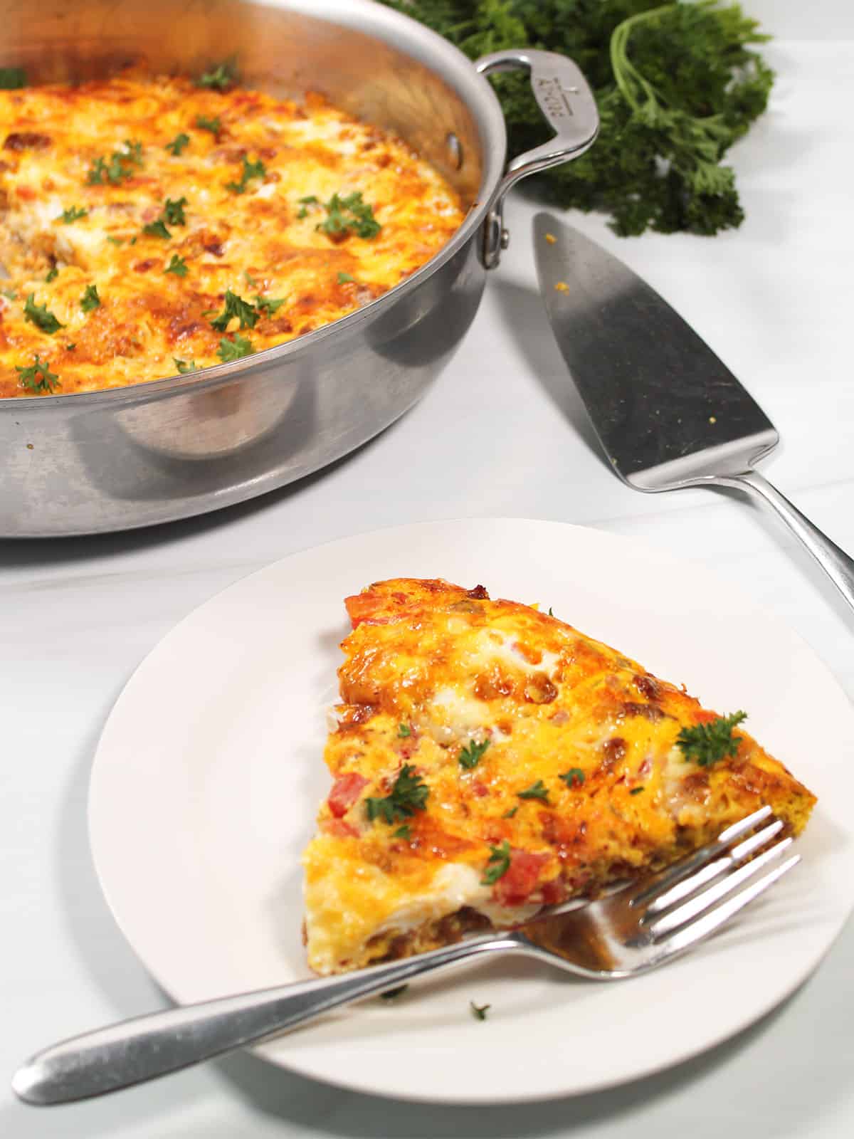 Slice of chorizo frittata on plate with skillet in back.