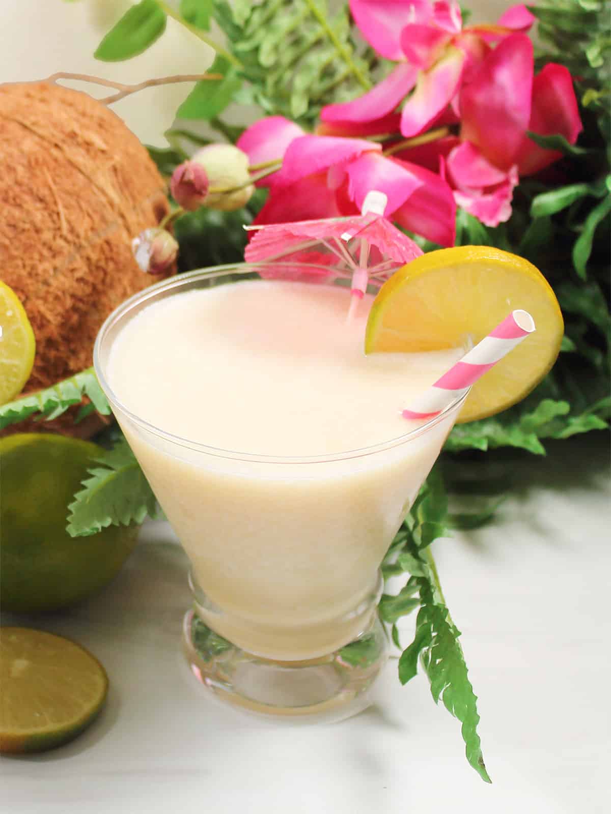One coconut daiquiri with lime wheel by coconut and flowers.