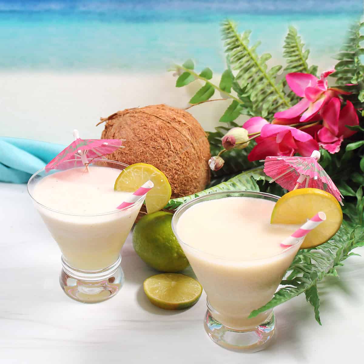 Two tropical coconut daiquiri cocktails beside coconut and flowers.