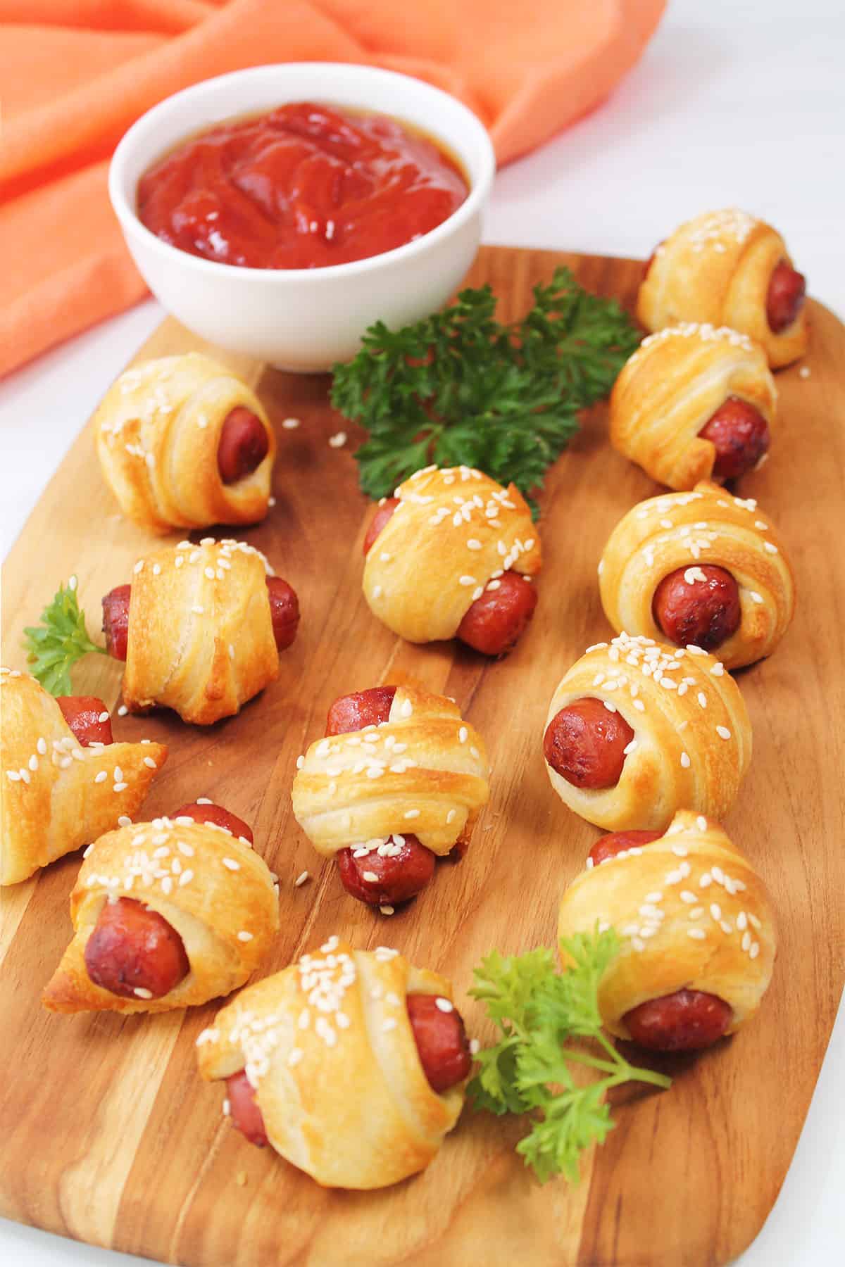 Serving air fryer pigs in a blanket on wooden board with dip.