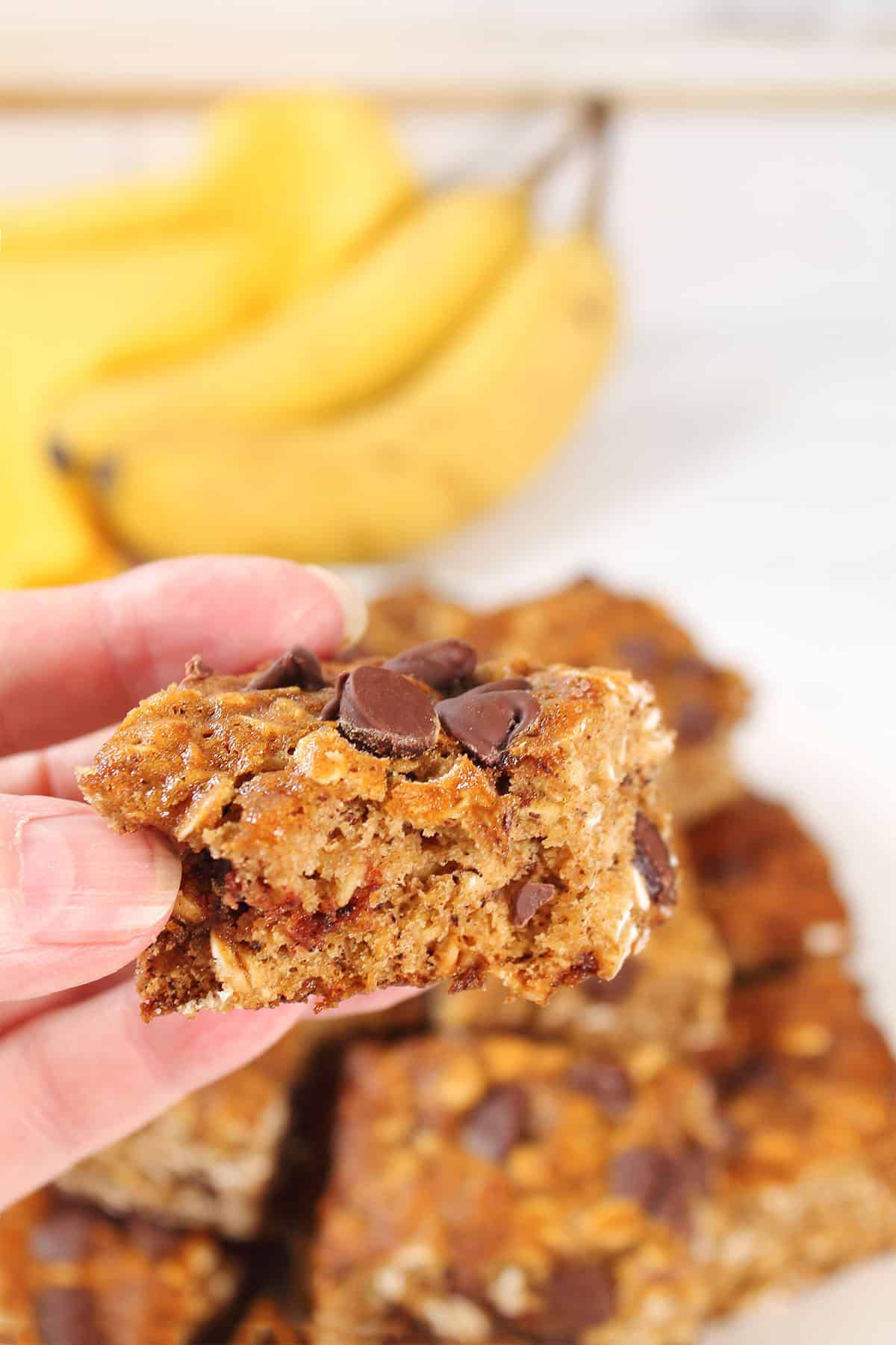 Holding banana oatmeal bar with bite out of it.