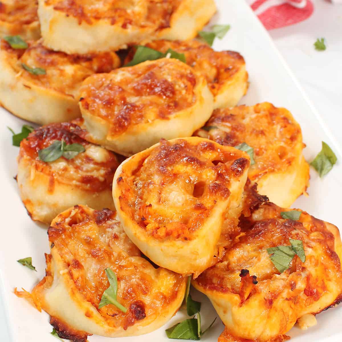 Chicken Parmesan Pinwheels on white platter with basil garnish.