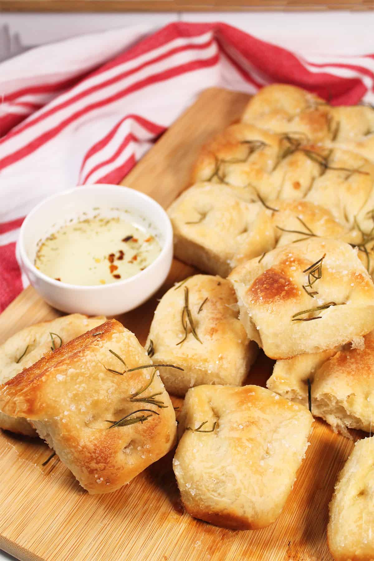 Focaccia bread with rosemary on wooden board with dipping oil.