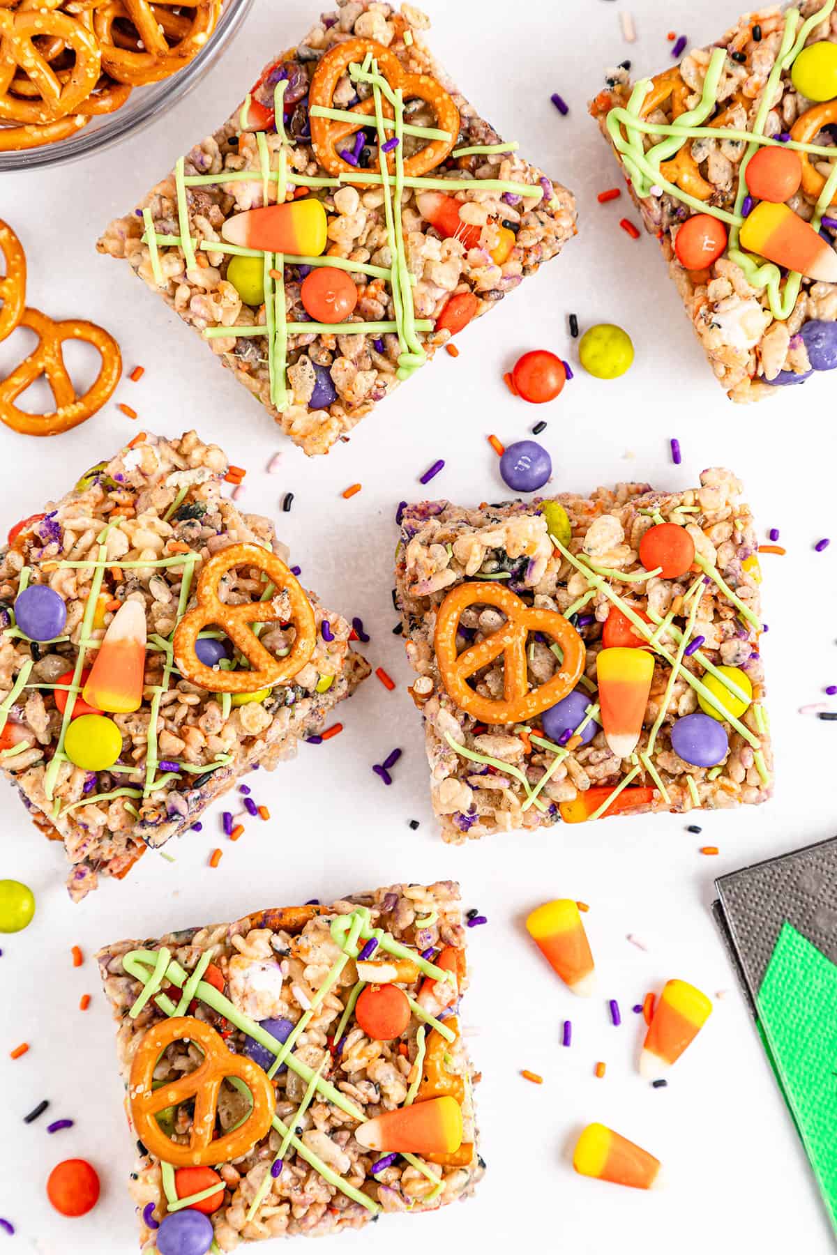 Rice Krispie Treats with Halloween candy and pretzels on white table.