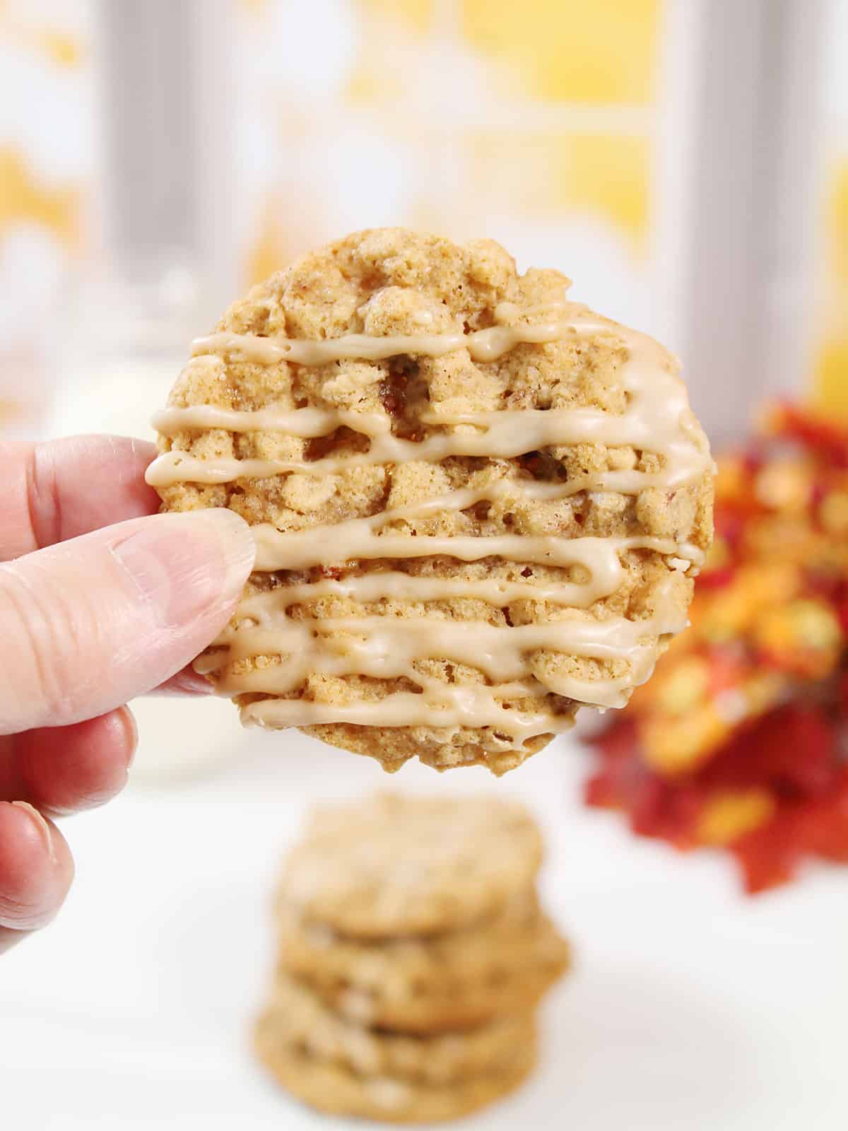 Holding an oatmeal cookie drizzled with maple icing.
